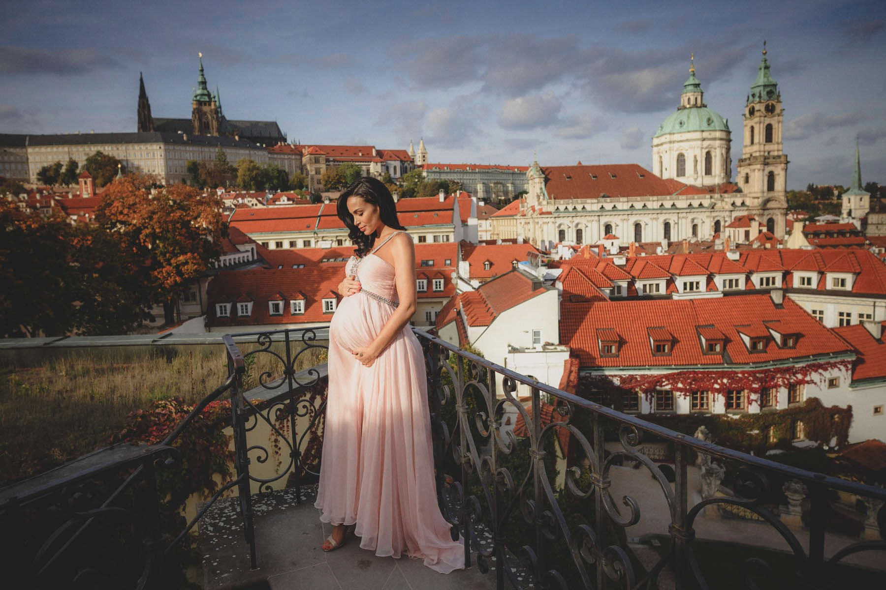 Pregnant woman in a pink gown on the upper terrace of Vrtba Garden above the Malá Strana rooftops