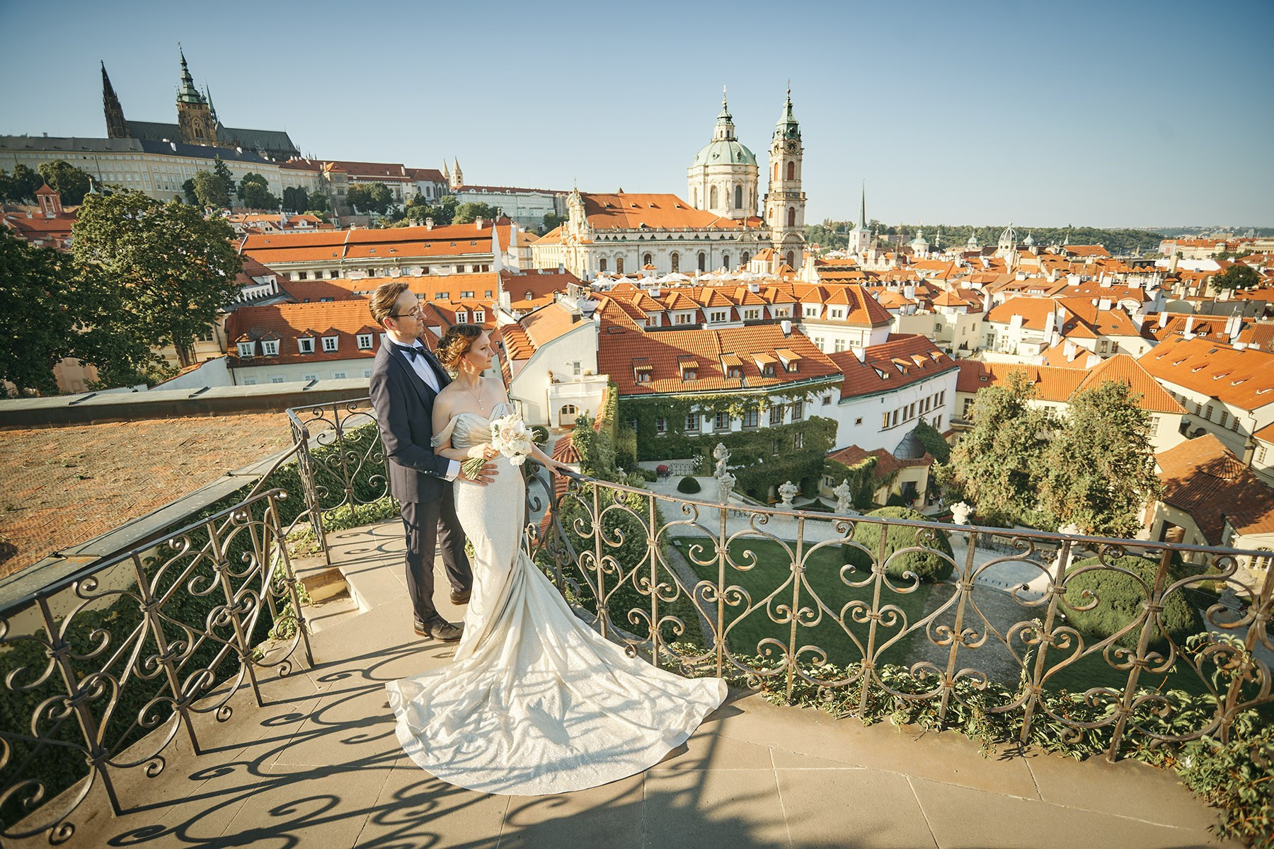 Ina and Vladimir on the upper terrace of Vrtba Garden, looking over Malá Strana rooftops toward St. Nicholas Church and Prague Castle.