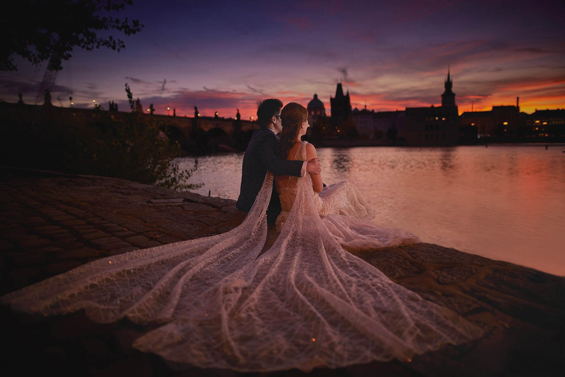 Stylish couple watching the sunrise by the Vltava River near Charles Bridge, Prague.