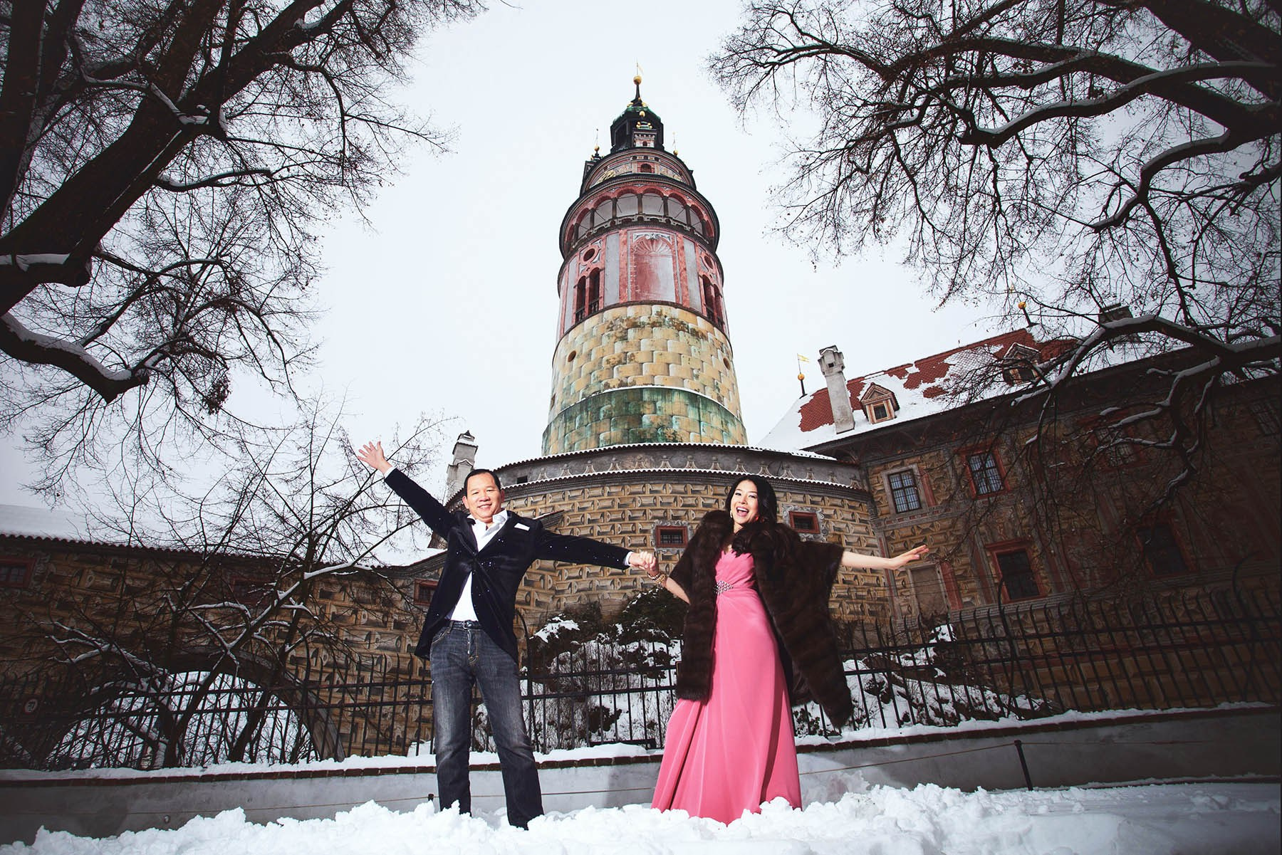Smiling CY and Helen pose under the Gothic tower at Český Krumlov Castle during their winter pre-wedding.