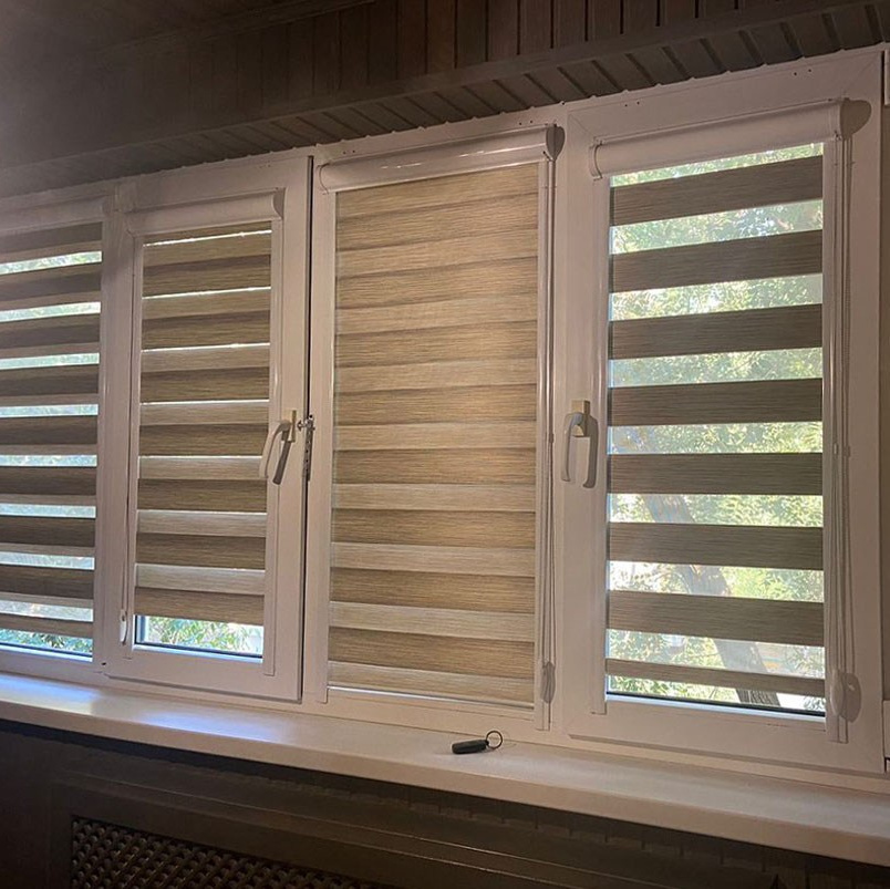 Рулонные жалюзи класса "день-ночь", установленные на большом пластиковом окне белого цвета.