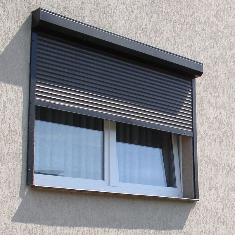 Белое пластиковое окно прикрыто полуопущенной коричневой роллетой.