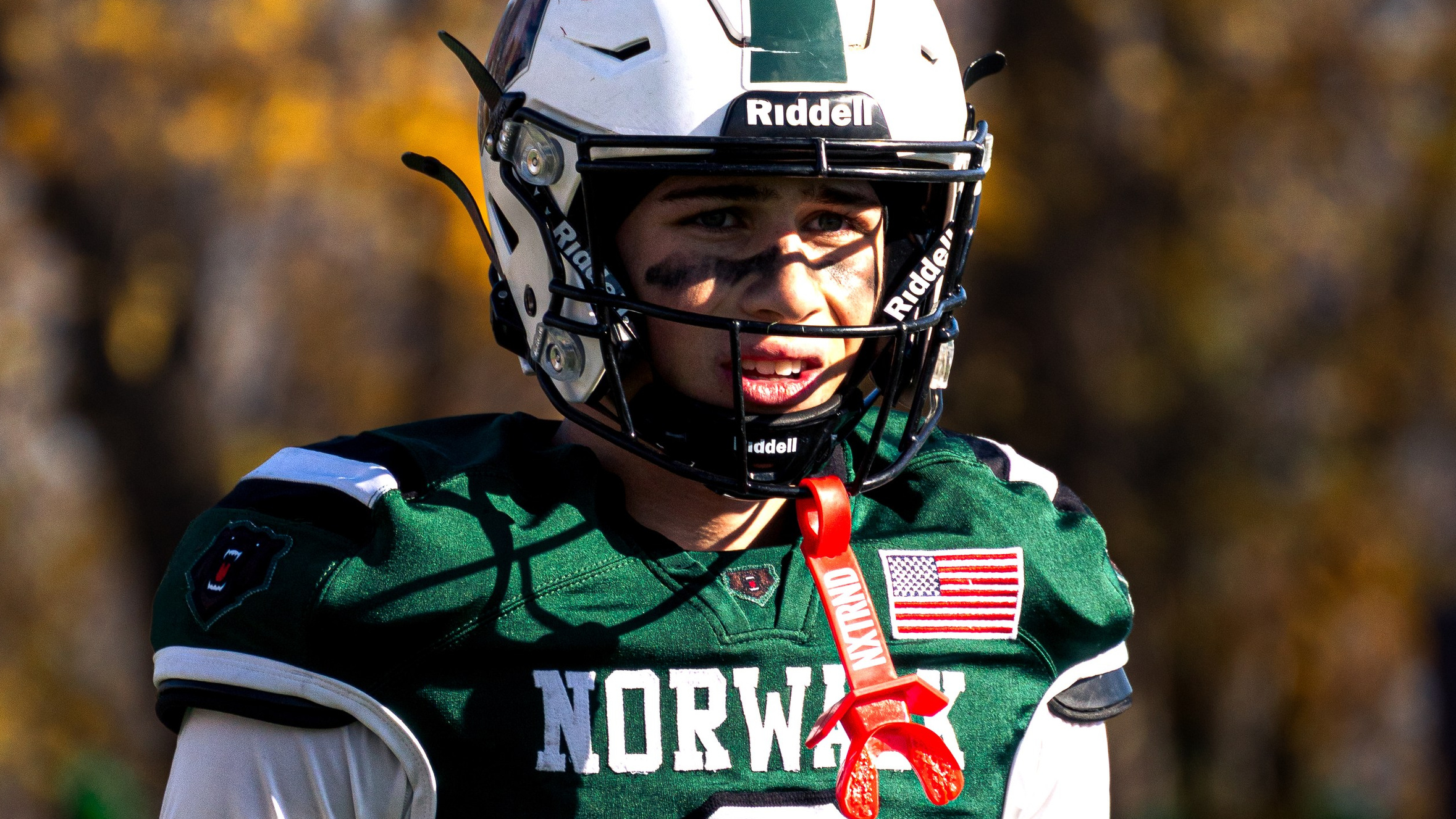 Portrait of a tired high school football player in a green uniform gazing downfield with an intense game-day expression.