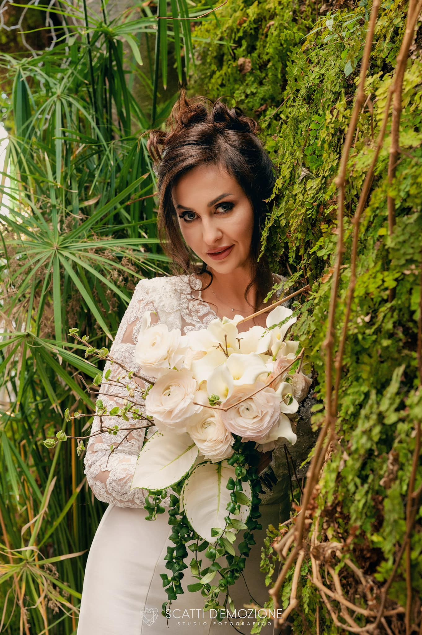 Sposa elegante in abito bianco con bouquet, fotografata su una strada antica di ciottoli circondata da verde lussureggiante, scatto professionale di matrimonio all'aperto