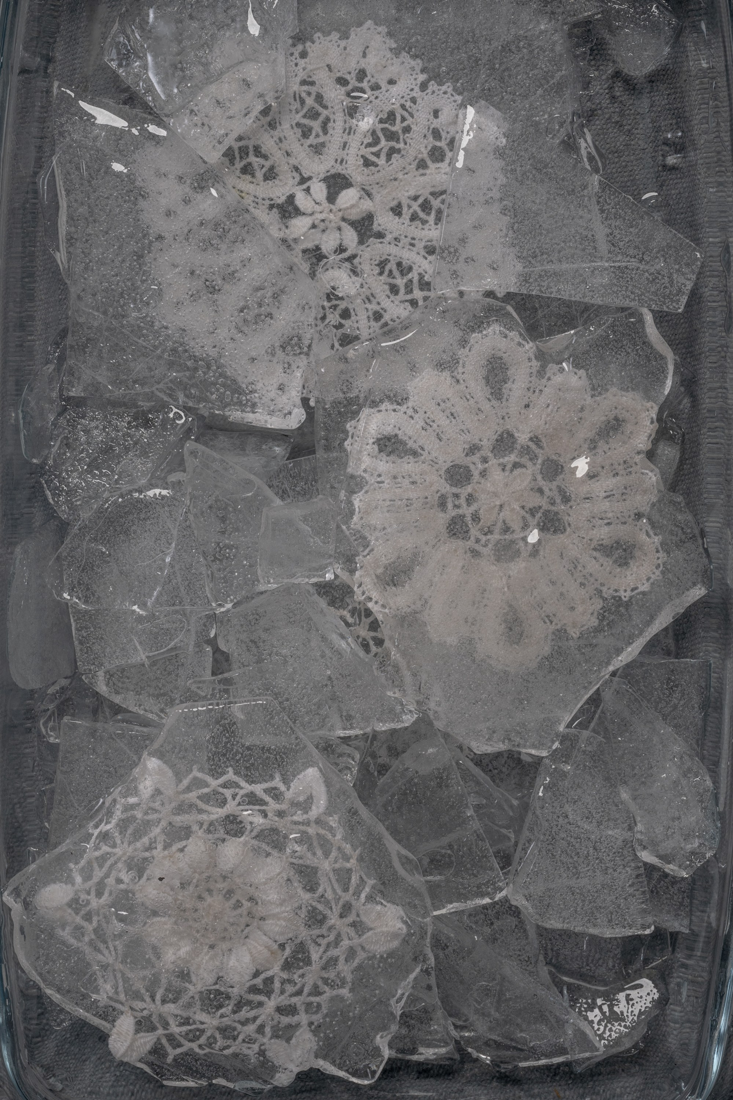 Fine art image of three lace doilies frozen in cracked ice, symbolizing emotional preservation, ancestral memory, and the silencing of feminine history – by Maria Tulchinskaya.