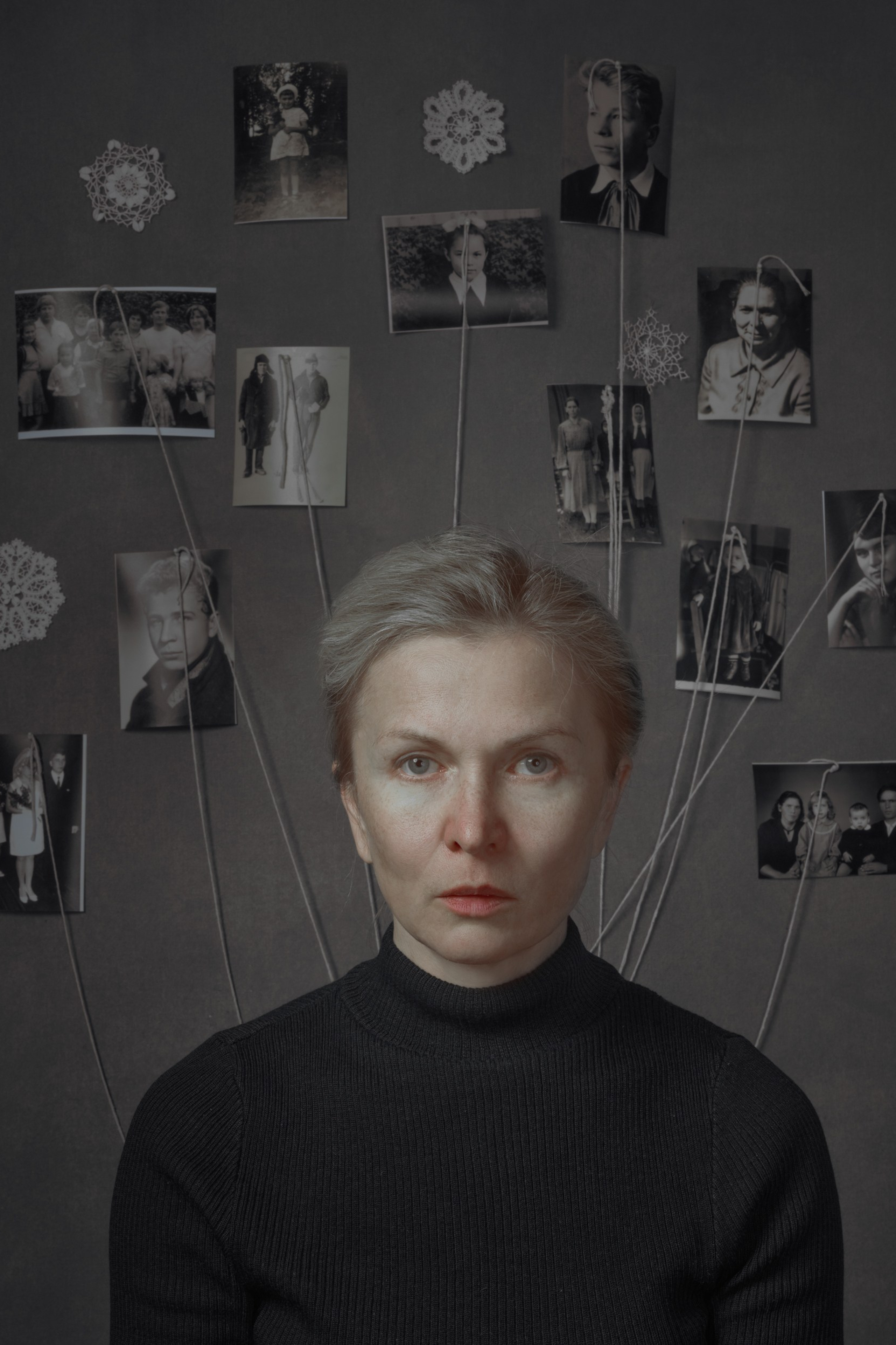 Portrait of a woman in black surrounded by vintage family photos connected with threads, symbolizing roots, inherited memory, and intergenerational presence – fine art photography by Maria Tulchinskaya