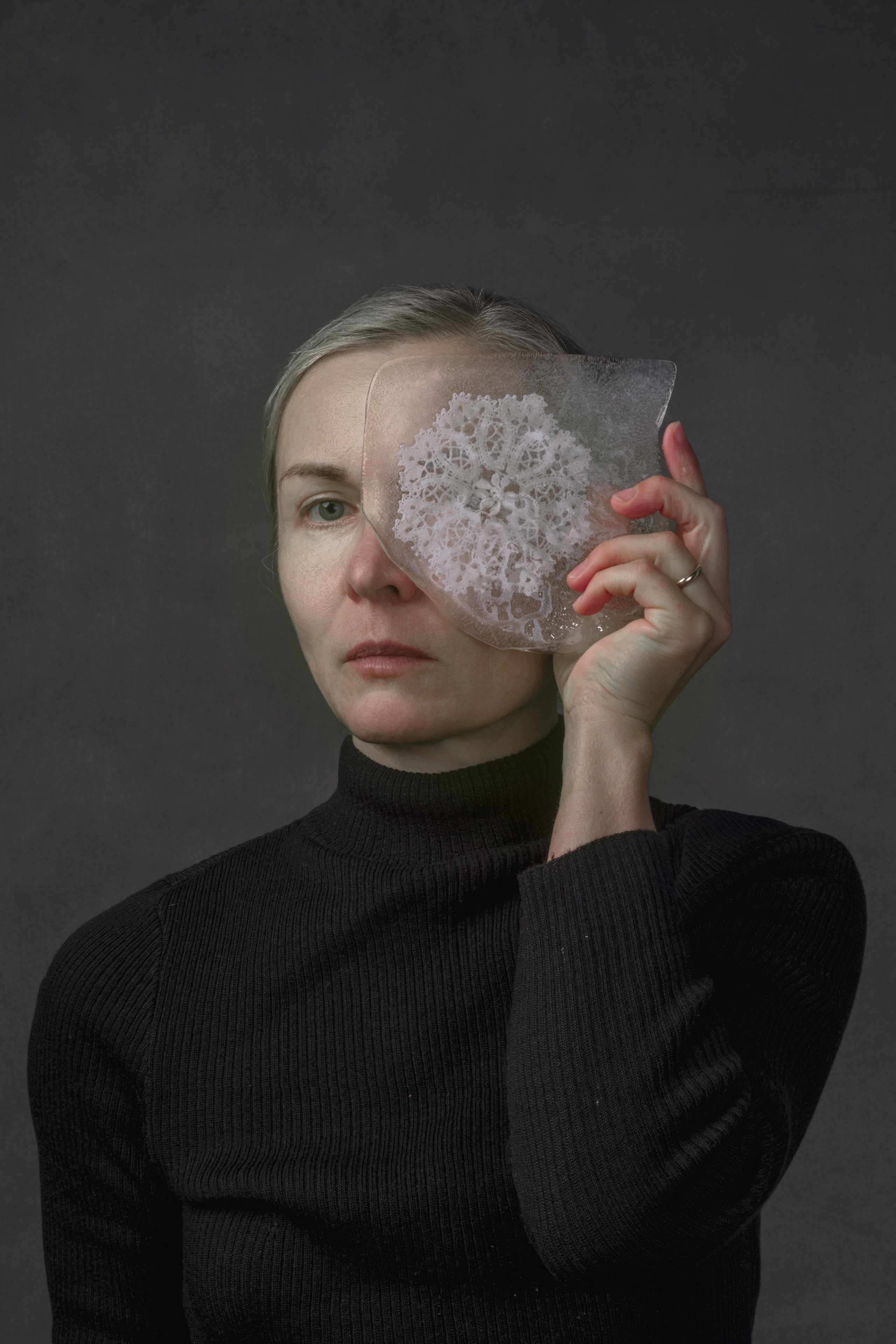 Portrait of a woman holding a shard of ice with frozen lace over one eye, symbolizing fragile memory, inherited silence, and dual perception – fine art photography by Maria Tulchinskaya.