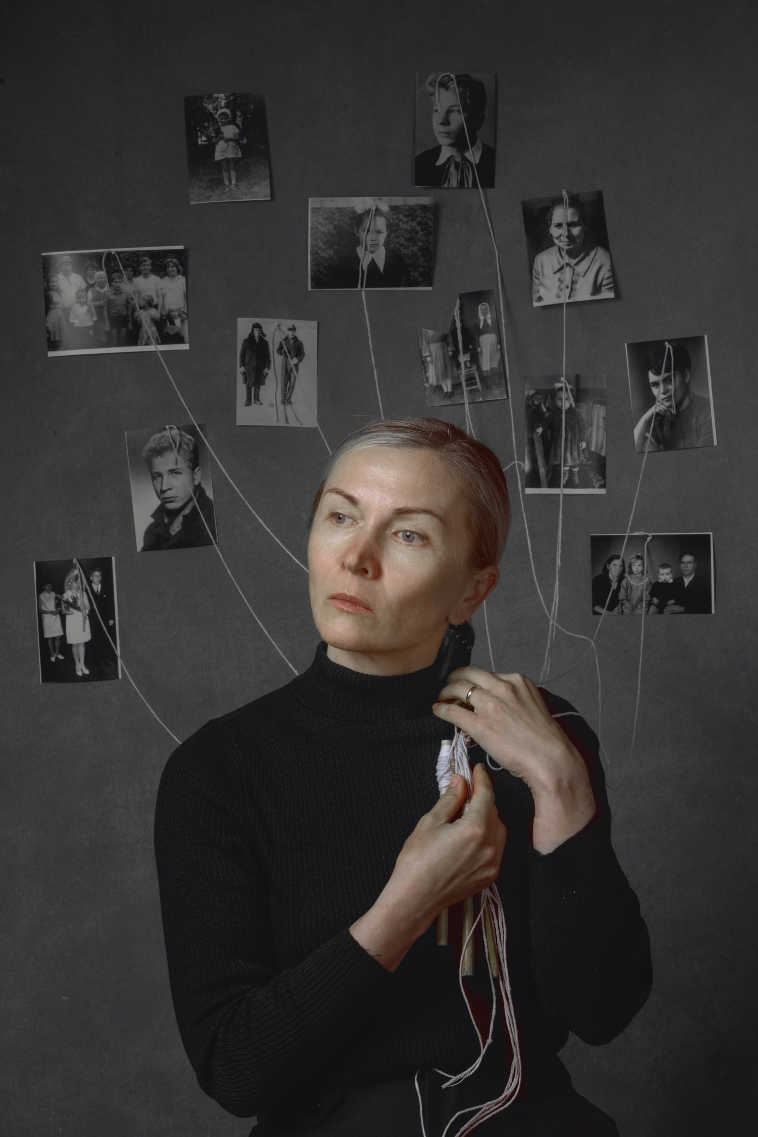 Portrait of a woman weaving threads into her hair, connected to vintage family photos around her, symbolizing emotional inheritance and intergenerational identity – fine art by Maria Tulchinskaya.