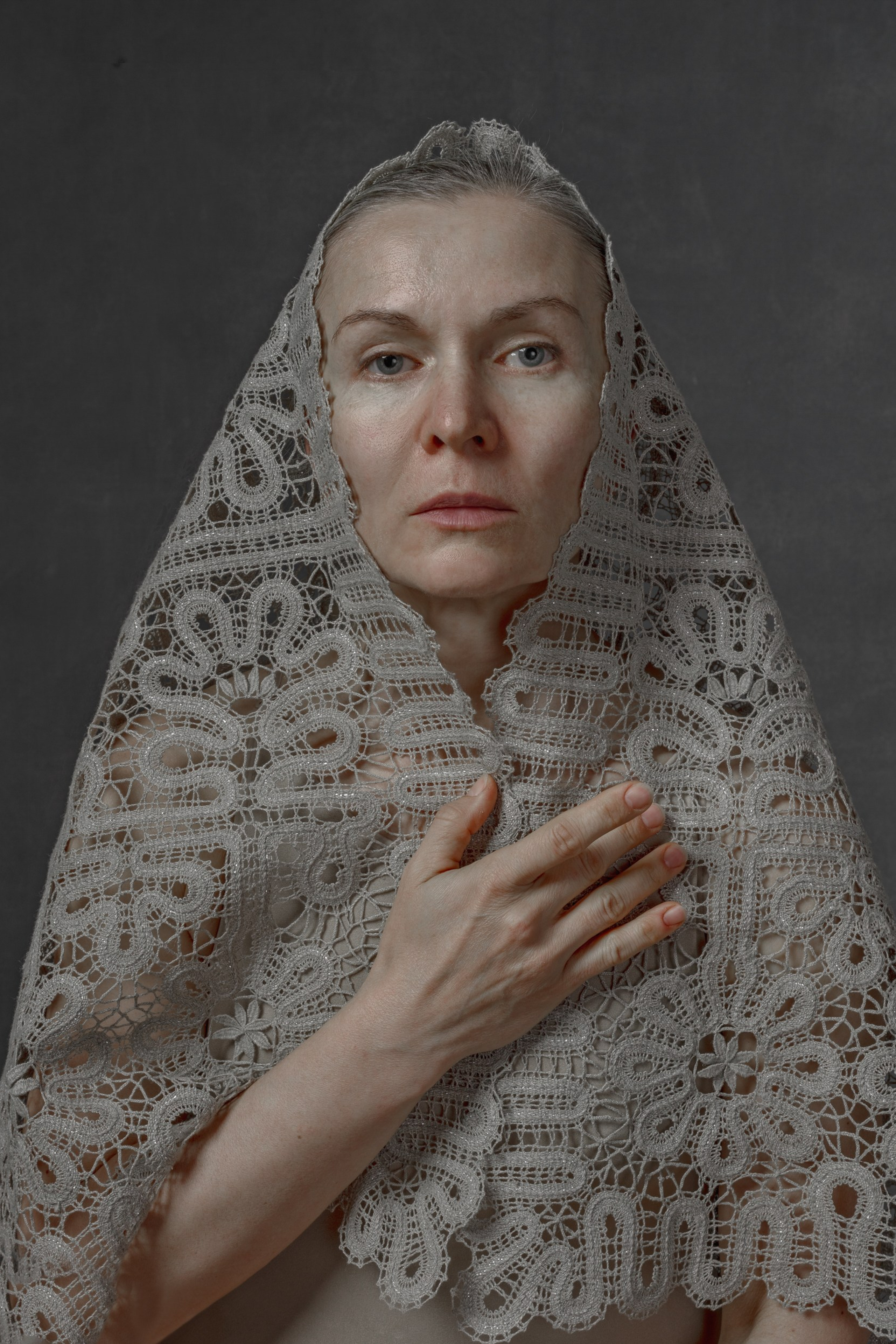 Portrait of a woman in handwoven lace veil, hand on chest, symbolizing memory, sacred femininity, and cultural heritage – fine art photography by Maria Tulchinskaya.