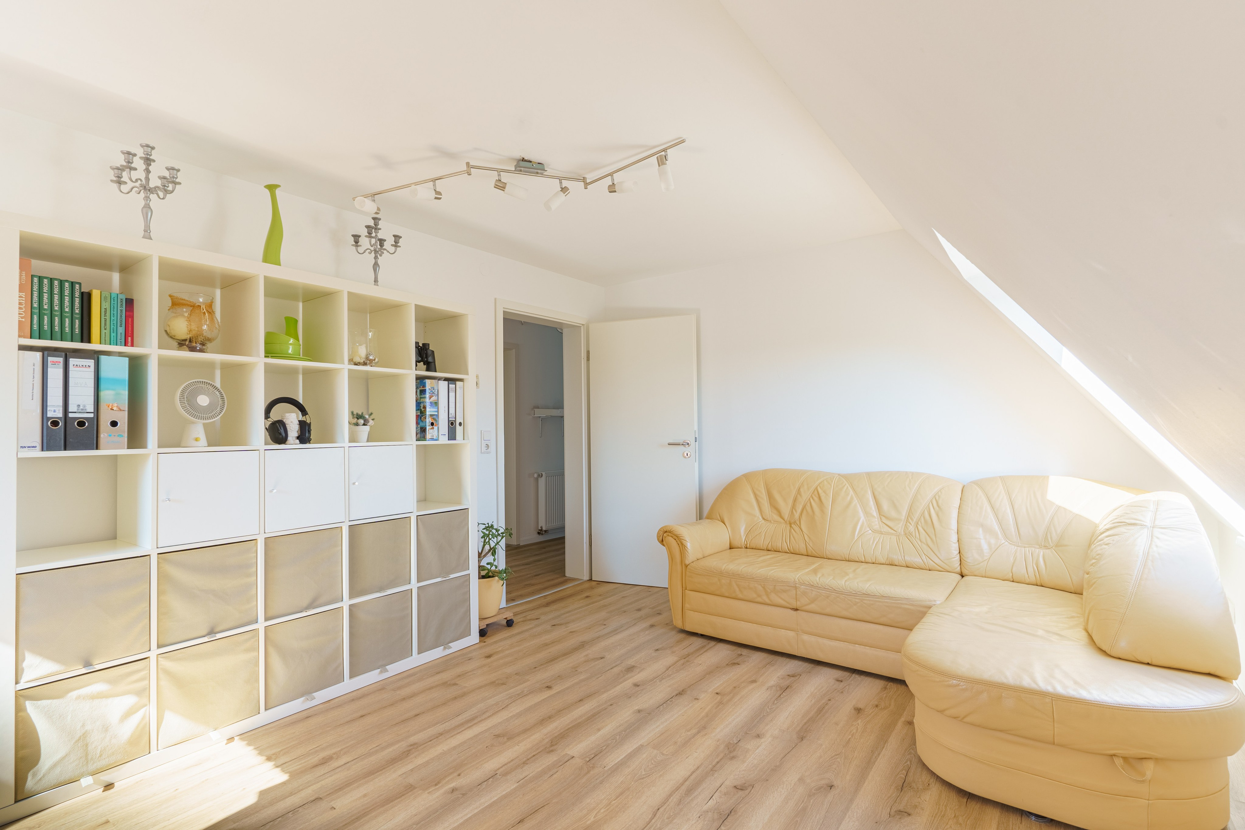 Originale Immobilienfotografie: Dachgeschosszimmer mit gelbem Ecksofa, großem Würfelregal und hellem Laminatboden. Fotografie von jade-visual.