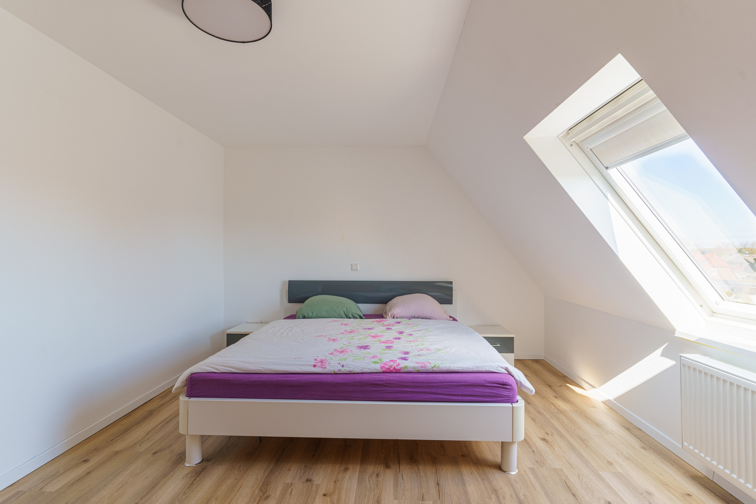 Originale Immobilienfotografie: Schlafzimmer im Dachgeschoss mit Doppelbett, Dachfenster und Laminatboden. Fotografie von jade-visual.