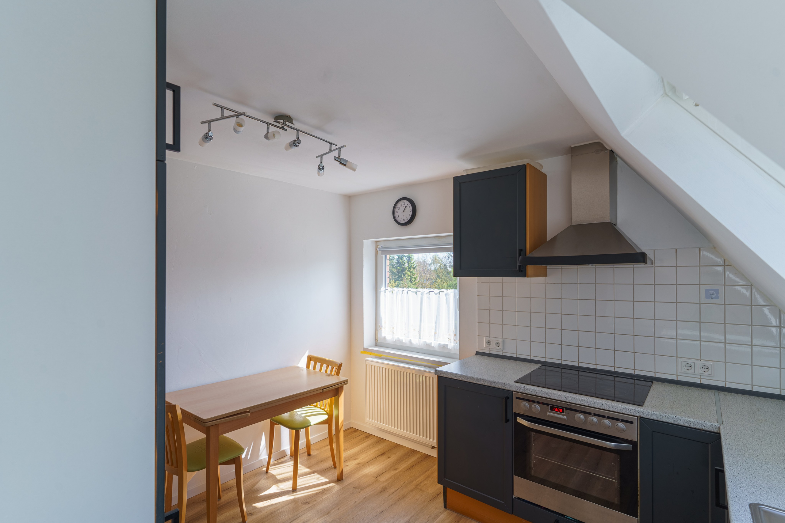 Originale Immobilienfotografie: Dachgeschossküche mit Kochfeld, Dunstabzugshaube und small Essbereich am Fenster. Fotografie von jade-visual.