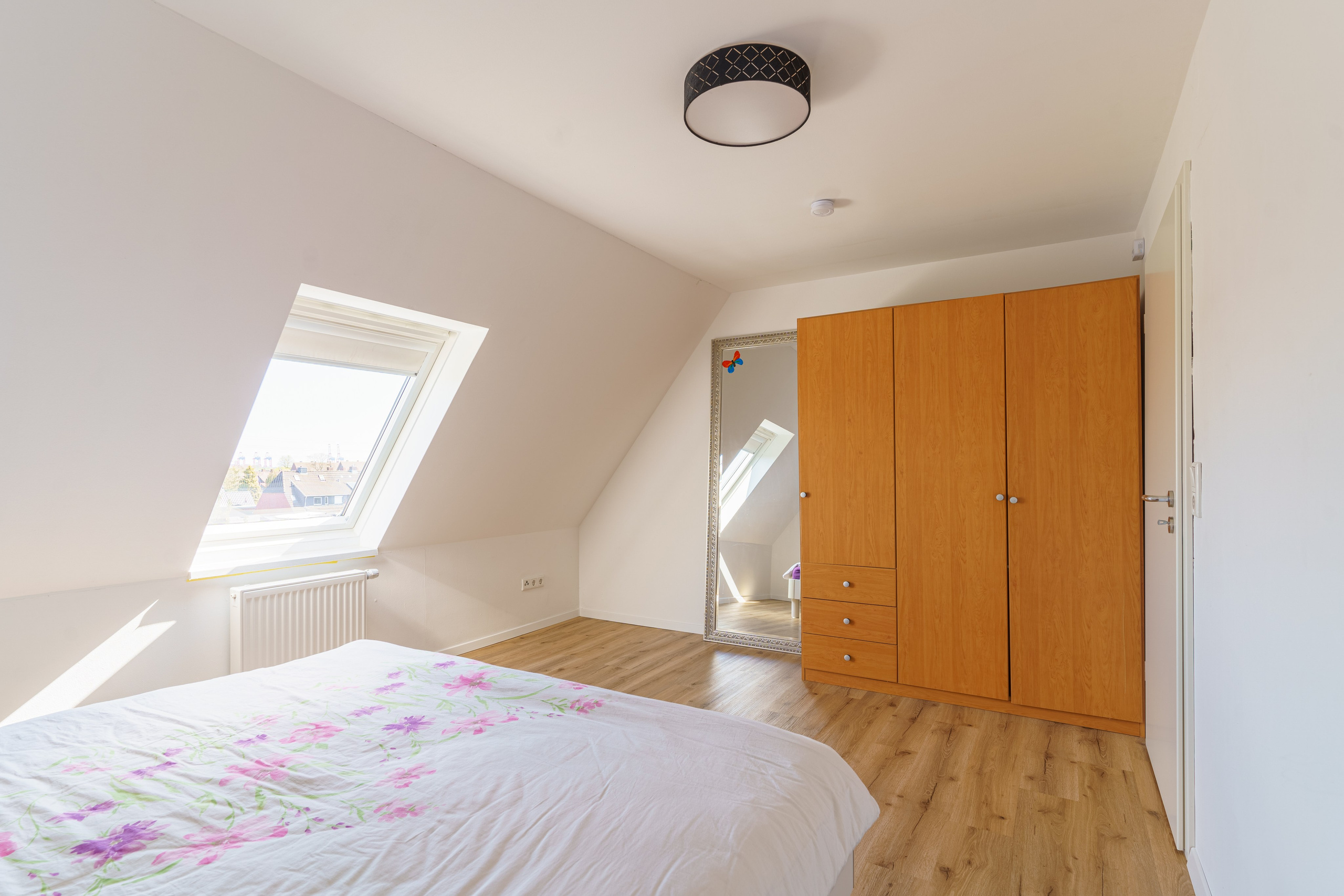 Originale Immobilienfotografie: Schlafzimmer im Dachgeschoss mit Holzschrank, großem Spiegel und Dachfenster. Fotografie von jade-visual.