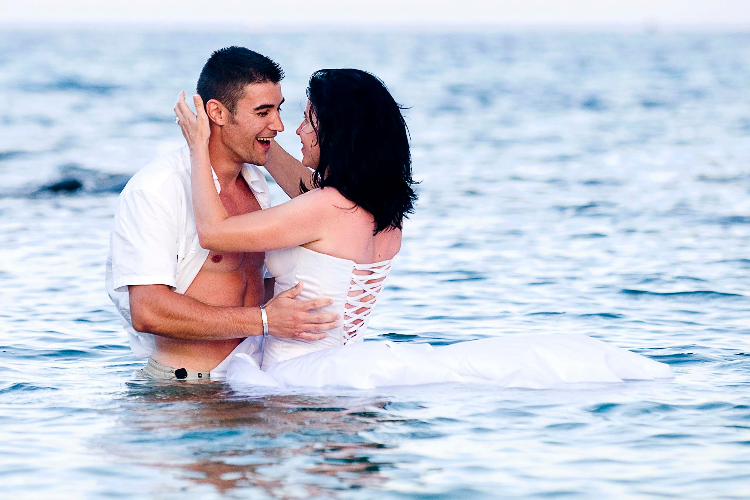 Bride and groom in wedding attire laughing together while standing in the Sea Vourvourou, Greece