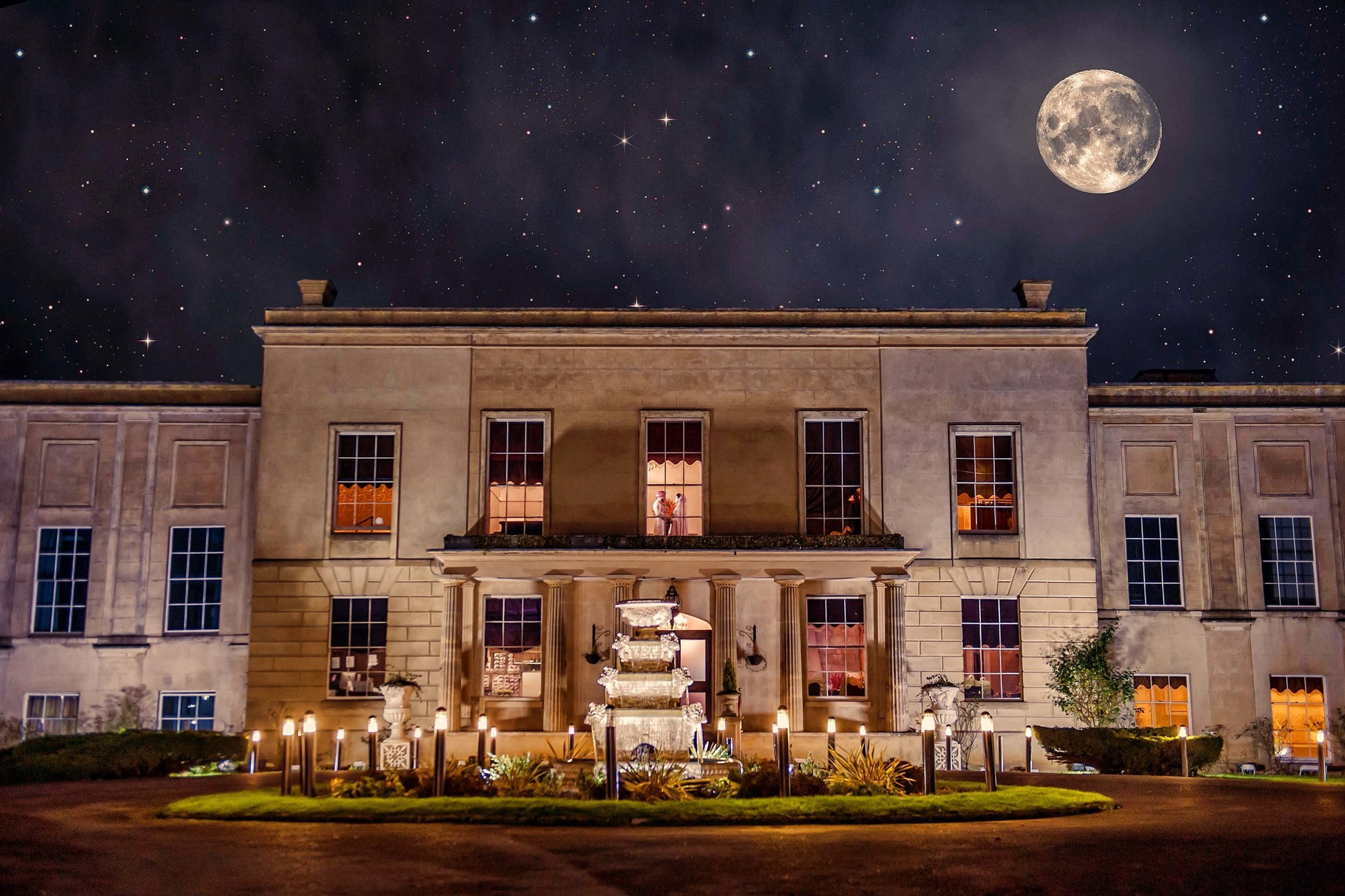 Bride and groom framed in the window of a grand mansion under a starry night sky with a full moon Newland Manor London, UK