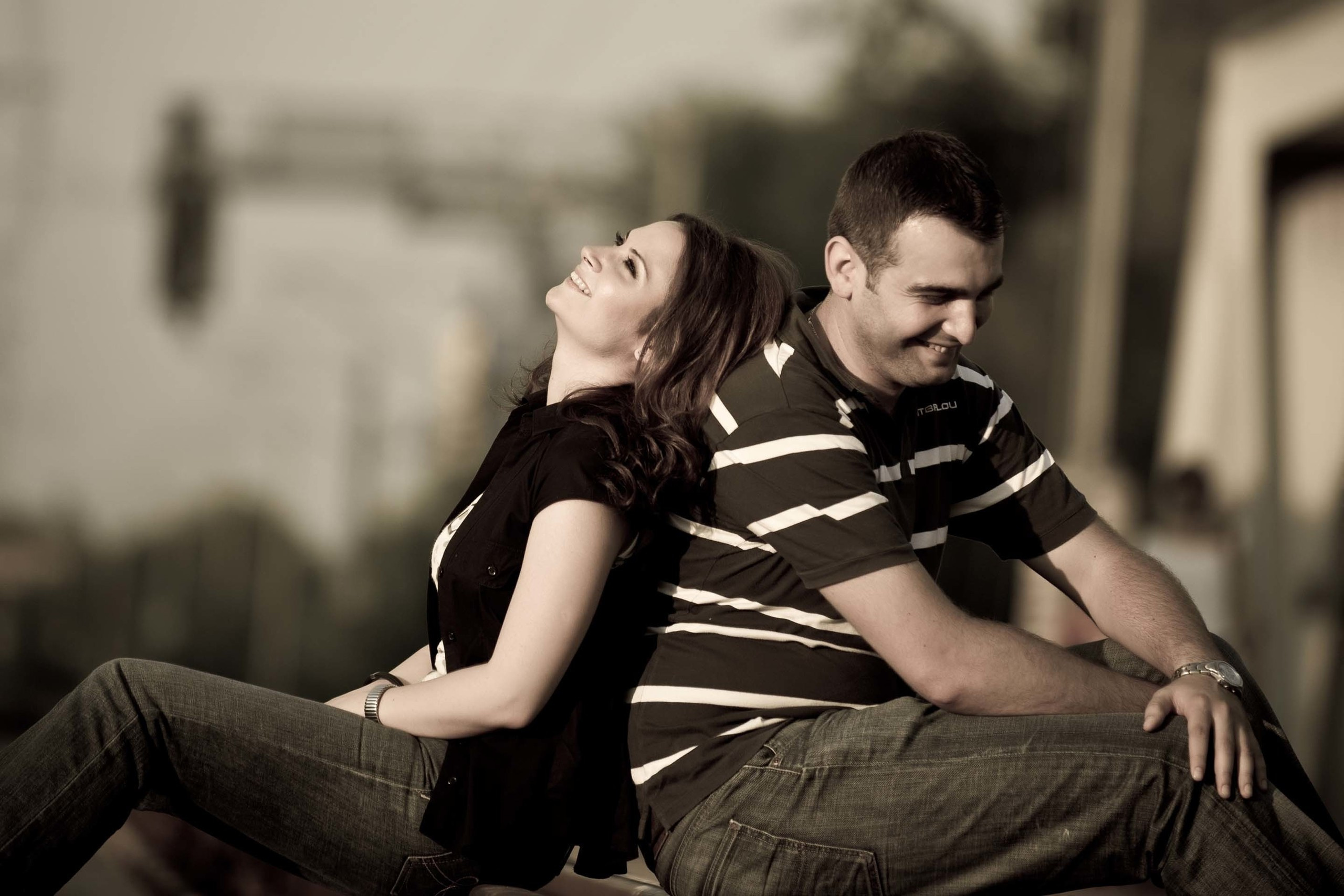 Couple in matching outfits sitting back-to-back and laughing on train tracks during creative engagement session
