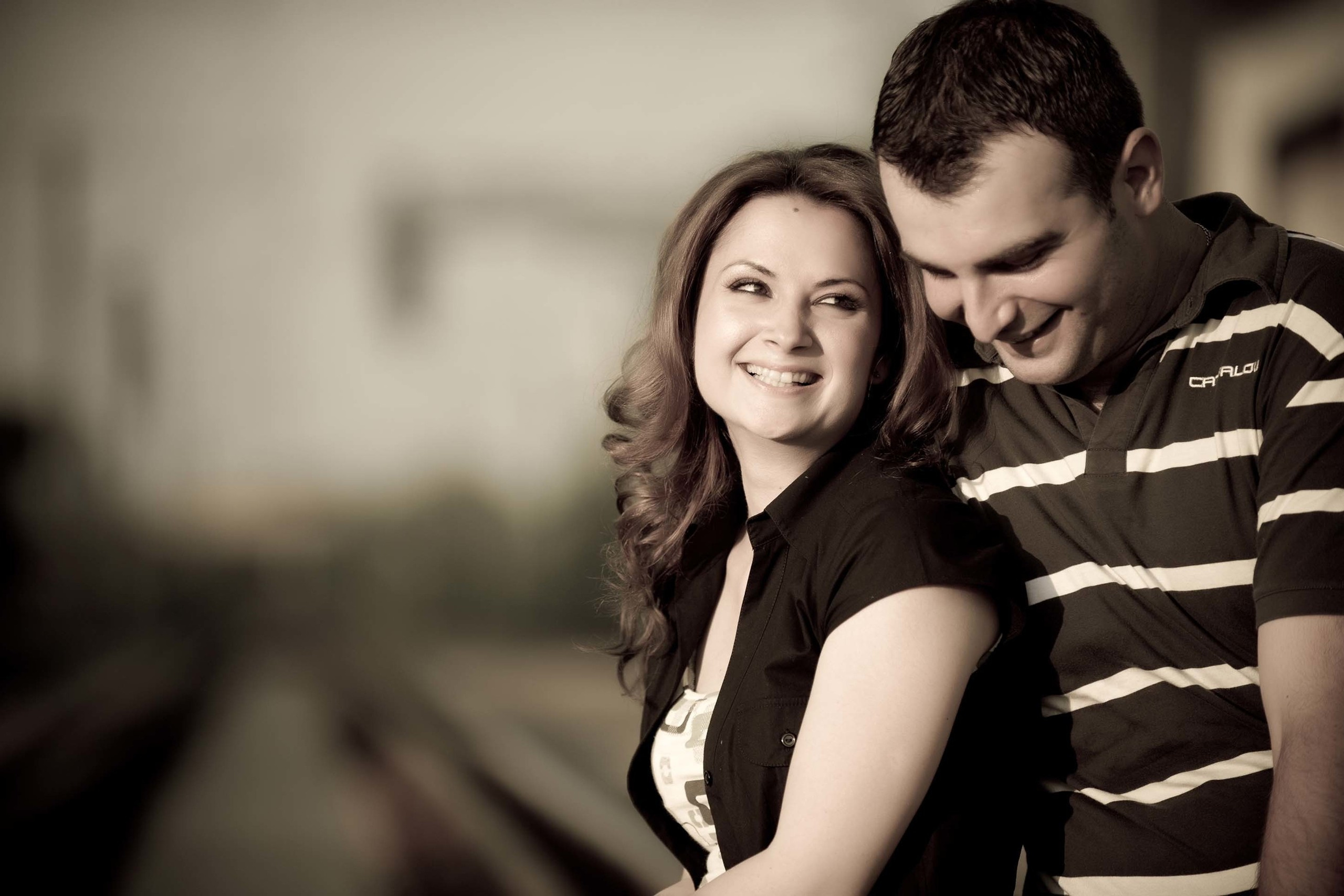 A couple sharing a candid moment laughing together in a sepia-toned vintage-style photo on a railway platform