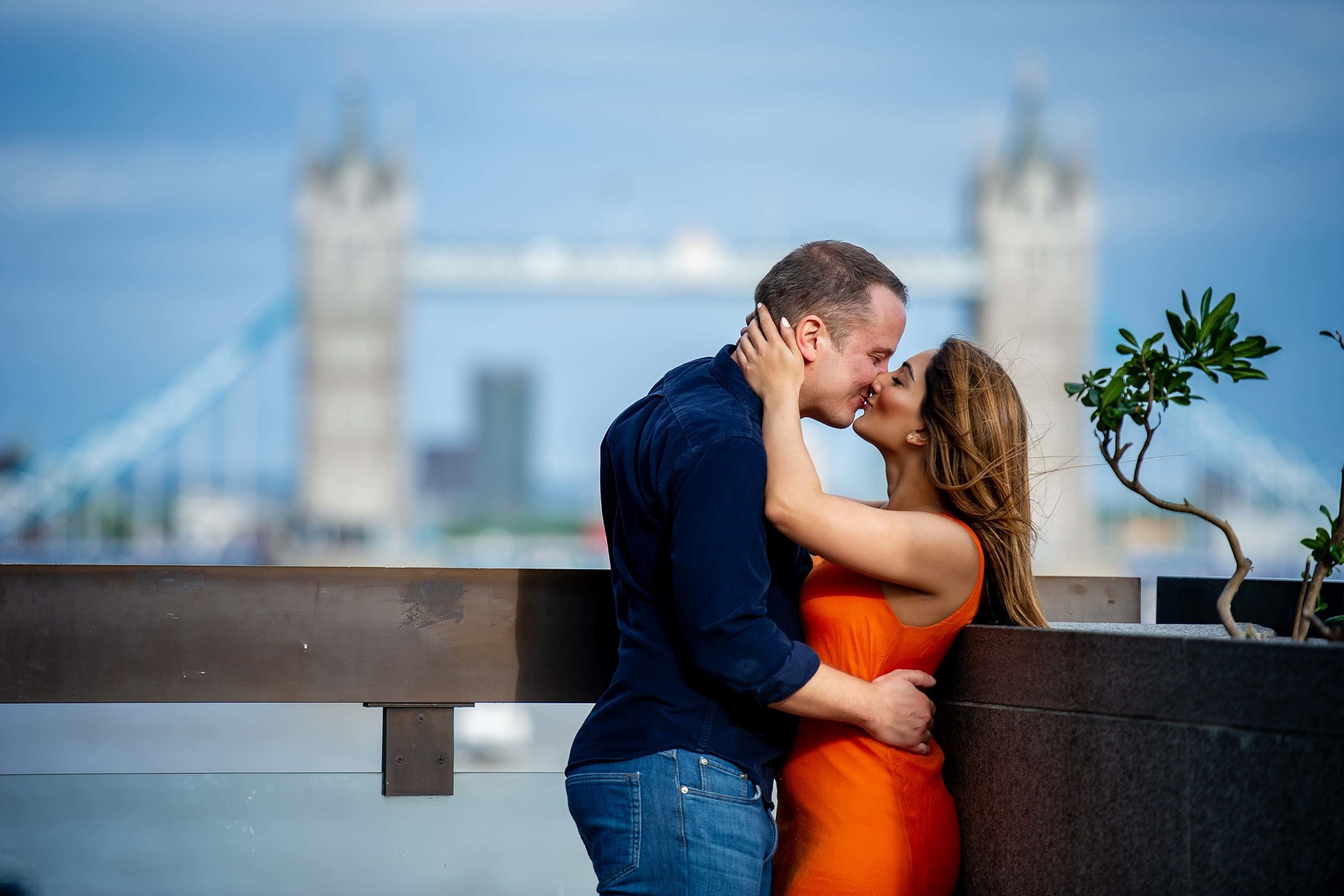 A couple kissing on a rooftop terrace with blurred Tower Bridge in the background