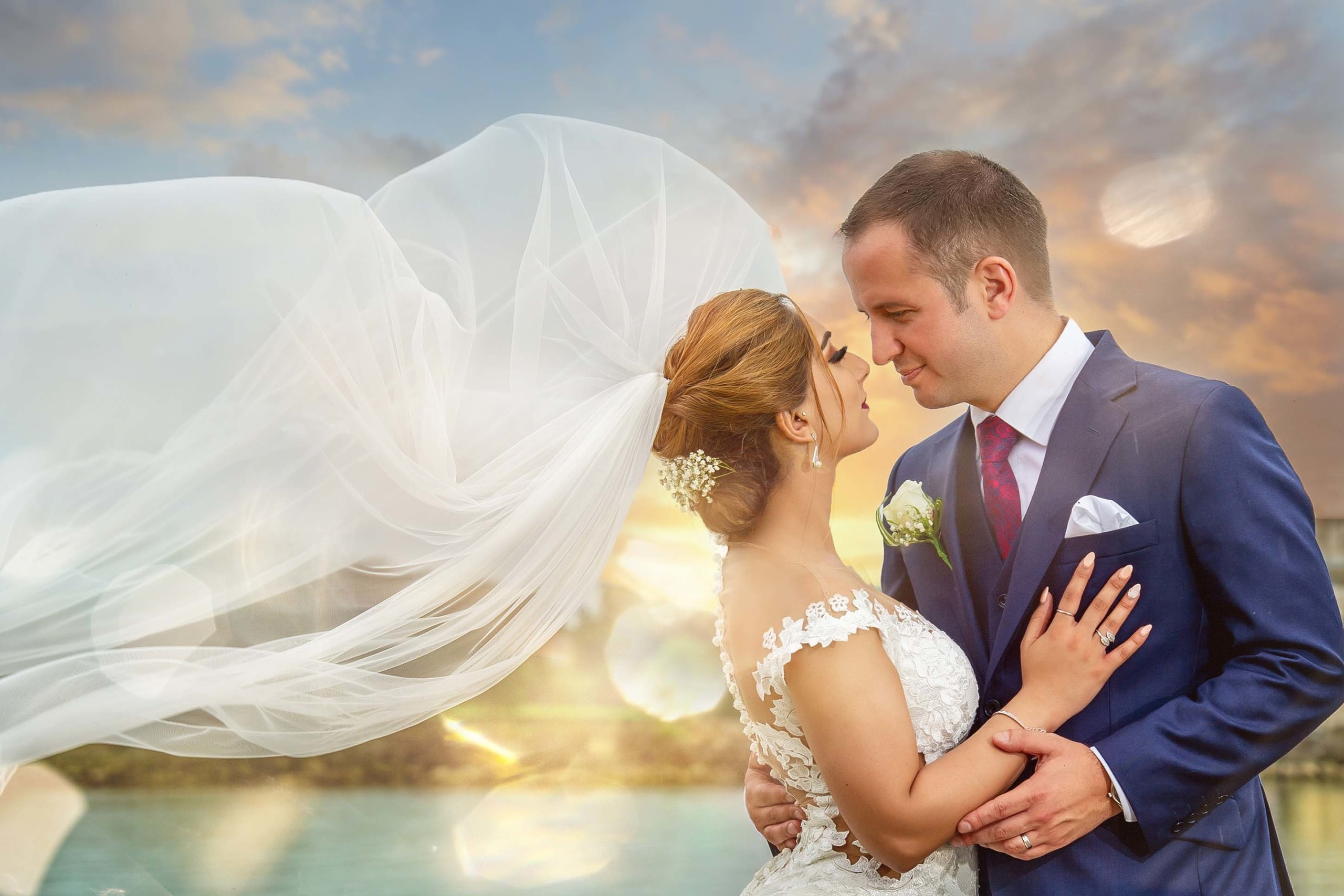 Bride with flowing veil embracing groom at sunset on their wedding day at Rutland Water, Leciester, UK