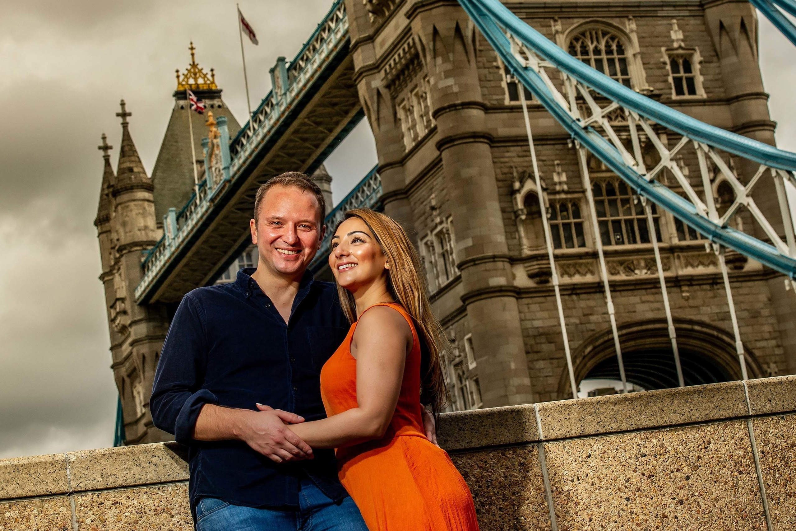 Smiling couple posing near Tower Bridge with an overcast sky