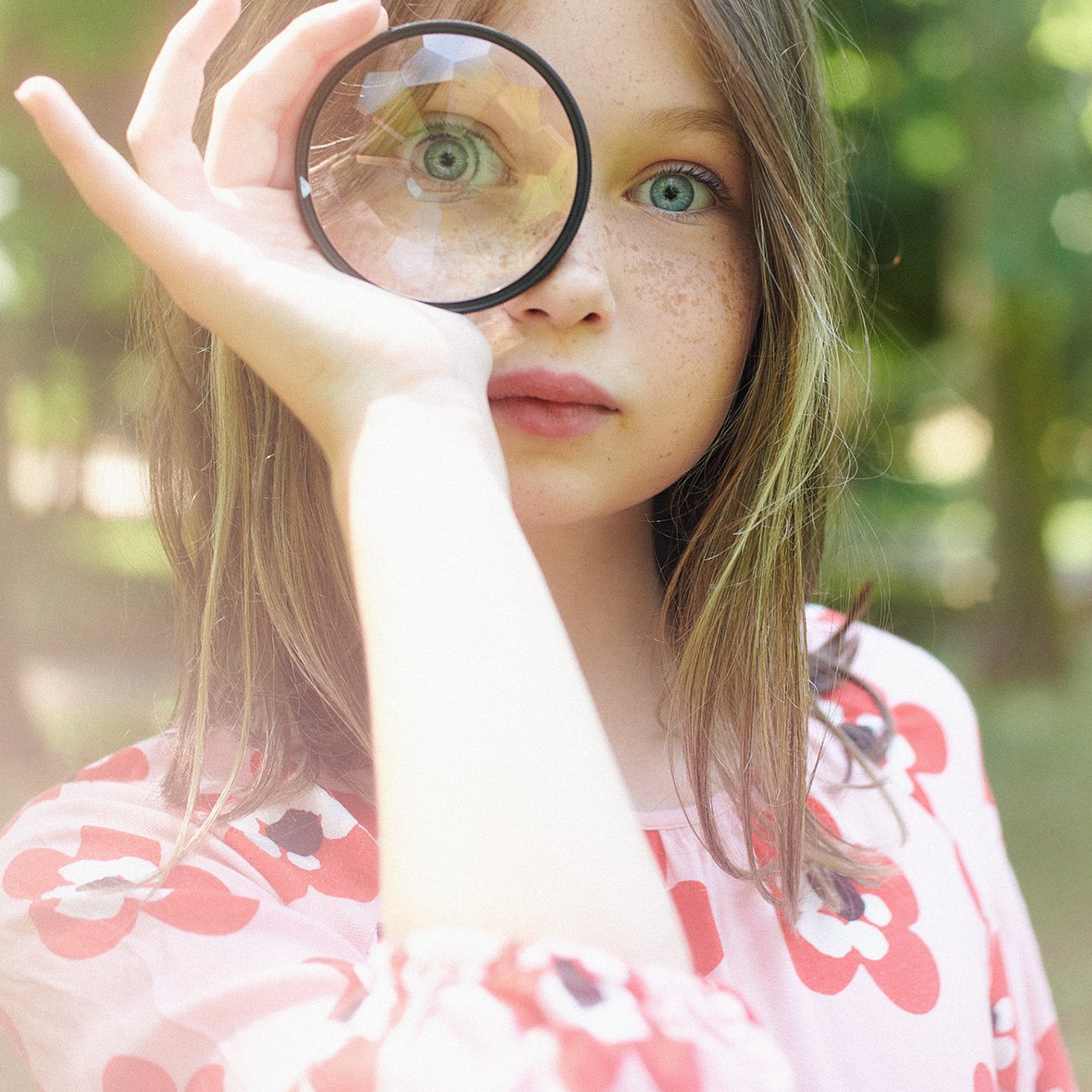 Portrait of a little blue-eyed girl exploring through a magnifying glass, children’s lifestyle photoshoot
