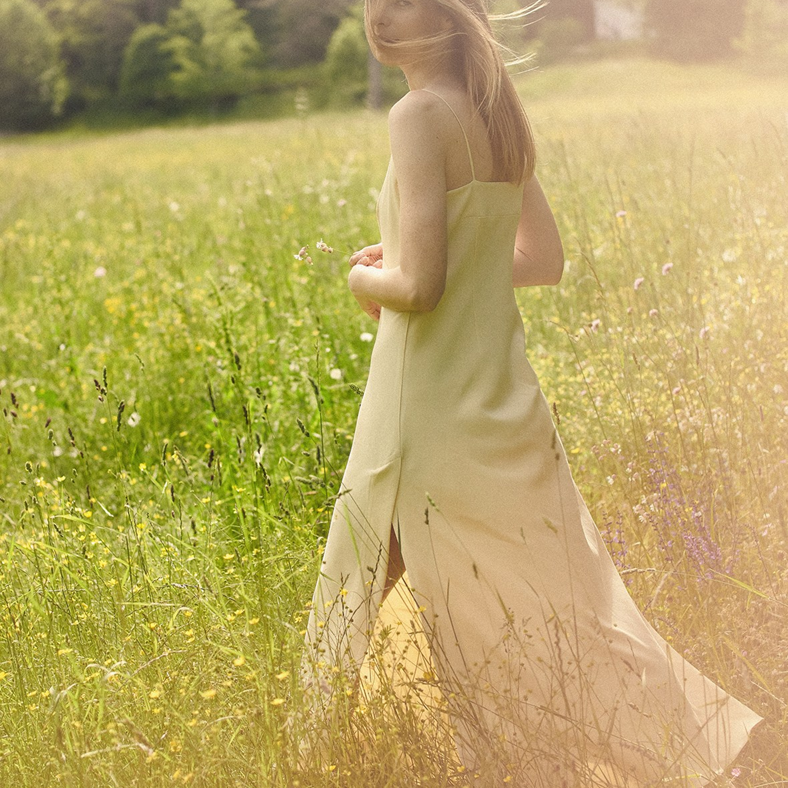 Fashion portrait of a woman in long yellow dress, photographed in a forest in soft light