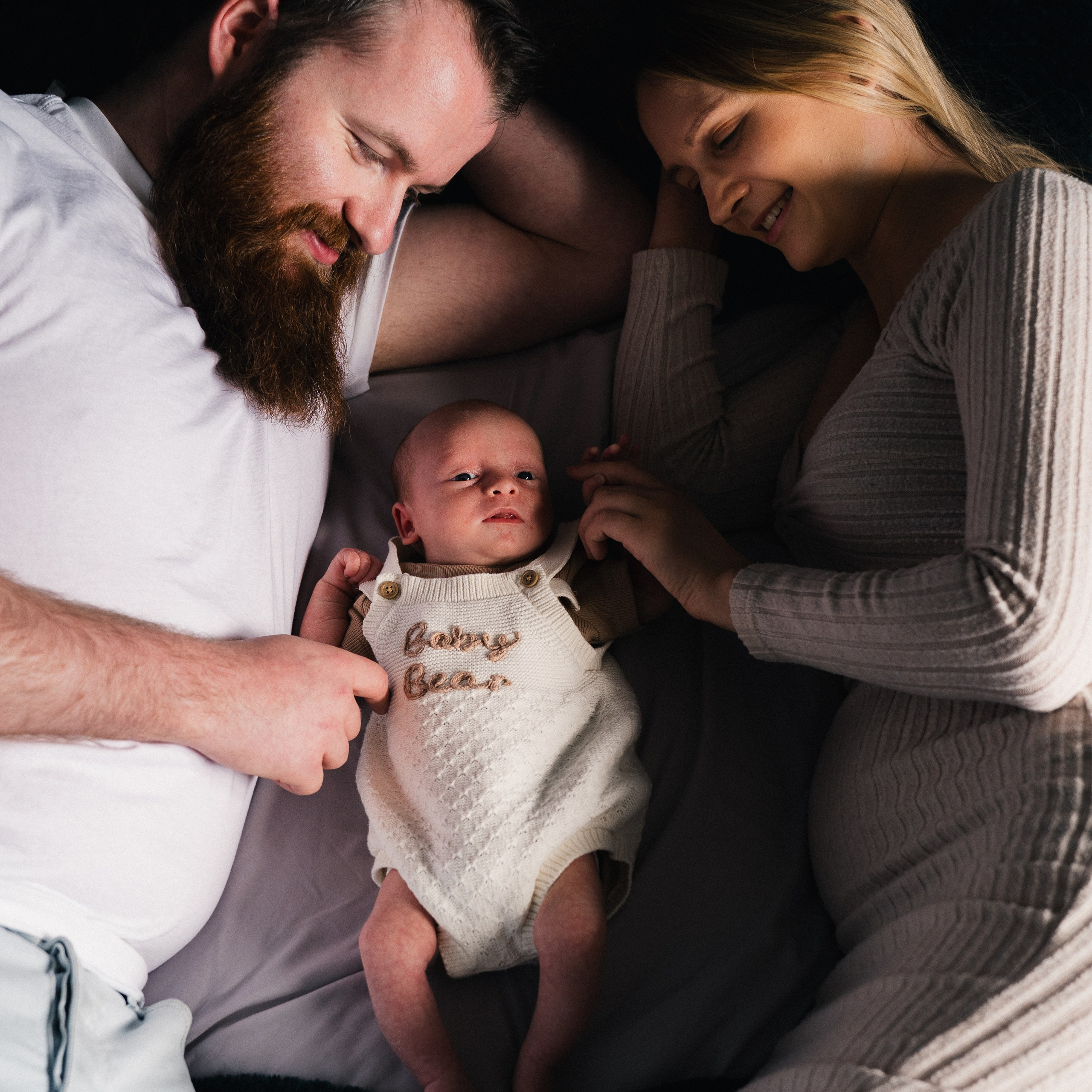 Newcastle newborn photographer photographing a father and a mother cuddling their sleeping newborn baby during a family newborn session.