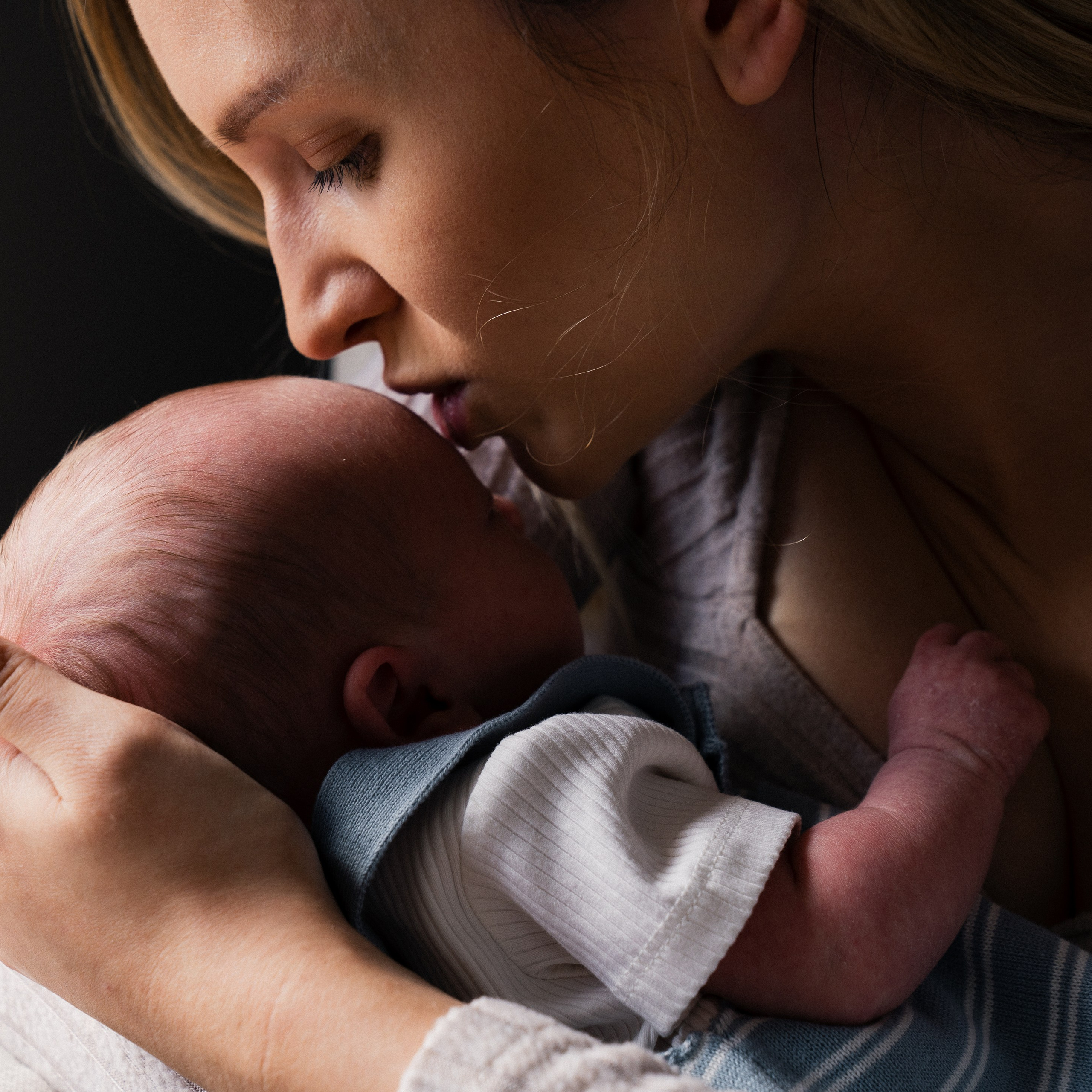 Bamburgh newborn photographer photographing a mother kissing her sleeping newborn baby during a family newborn session.
