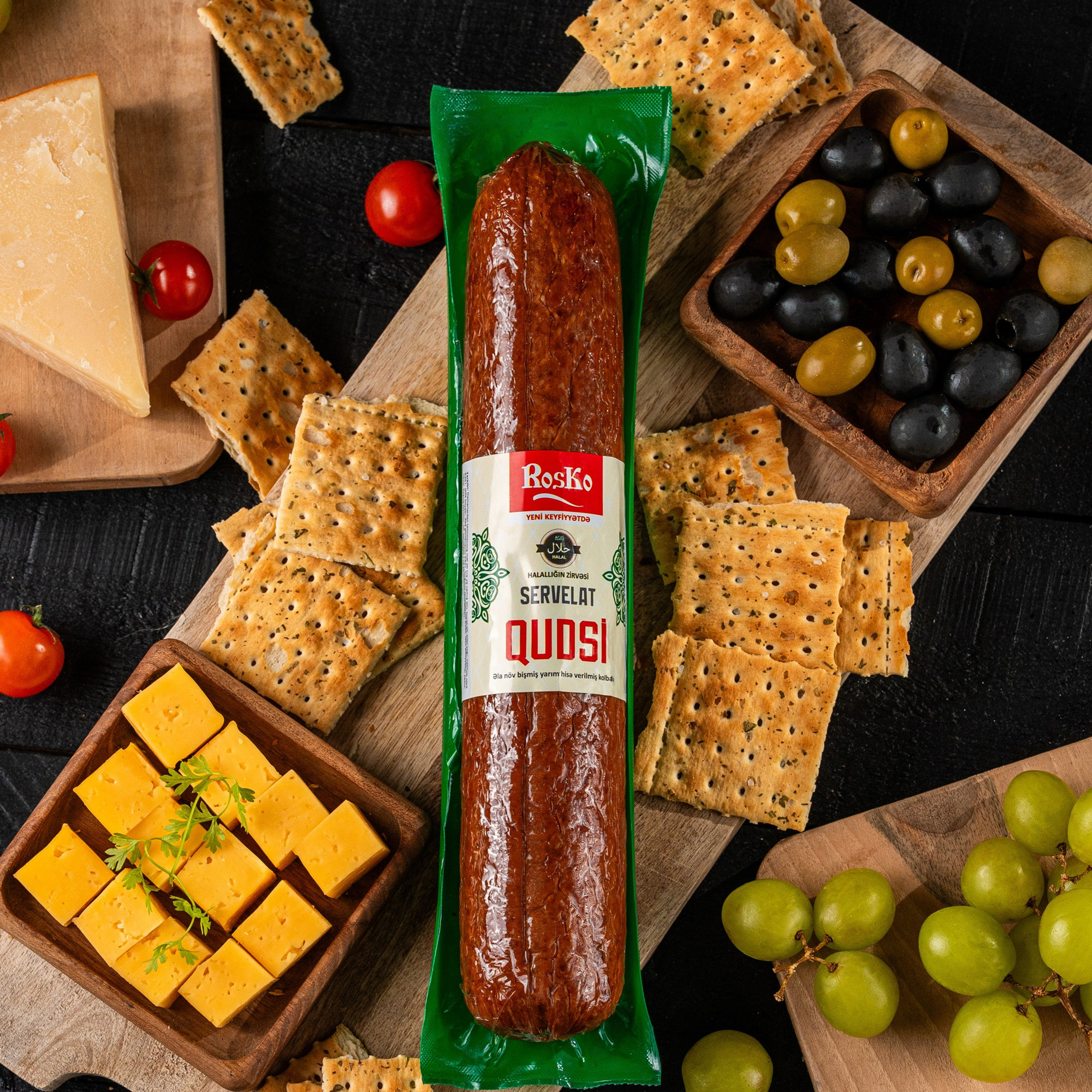 Roska “Qüdsü” servelat kolbasası pendir kubları, yaşıl və qara zeytun, yaşıl üzüm və duzlu krekerlərlə zəngin qida tərtibatında.