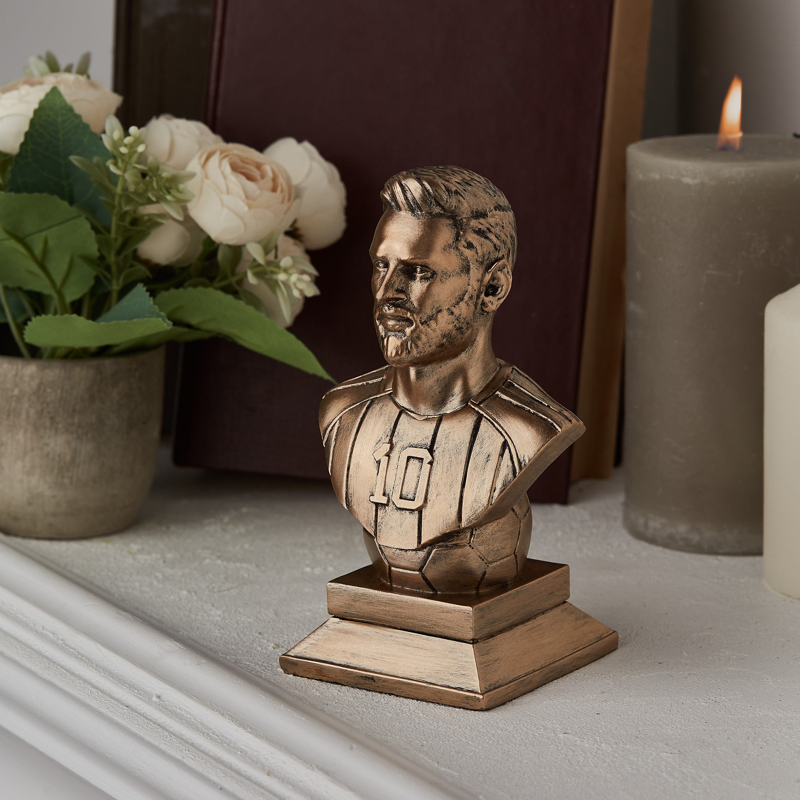 Lionel Messinin bürünc büstü, divan üzərində güllər, şamlar və kitablar arasında, dekorativ kompozisiyada.