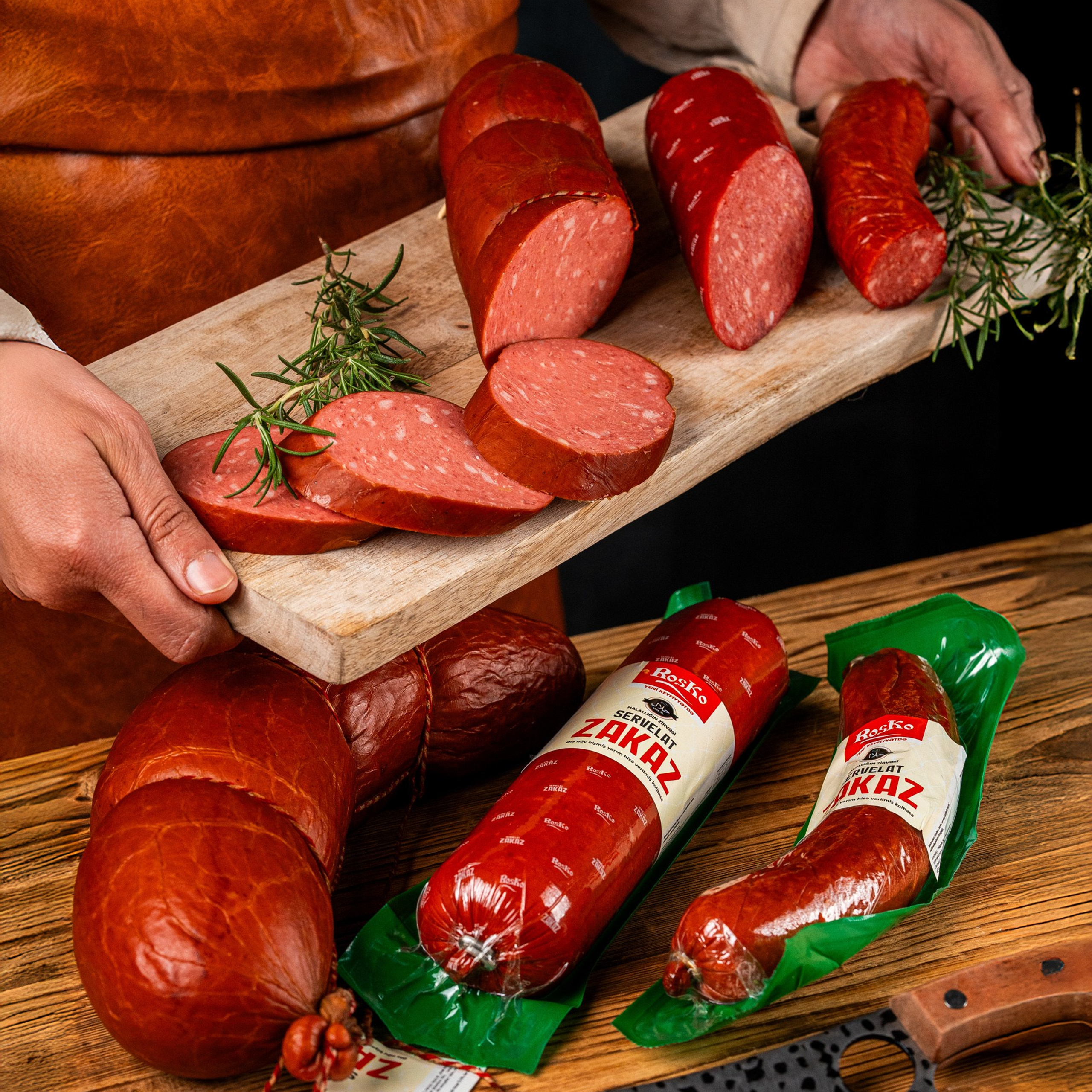 Roska “Zakaz” servelat kolbasası dilimlənmiş formada, ustanın əlində kəsim taxtasında, paketli variantlarla birlikdə təqdim olunub.