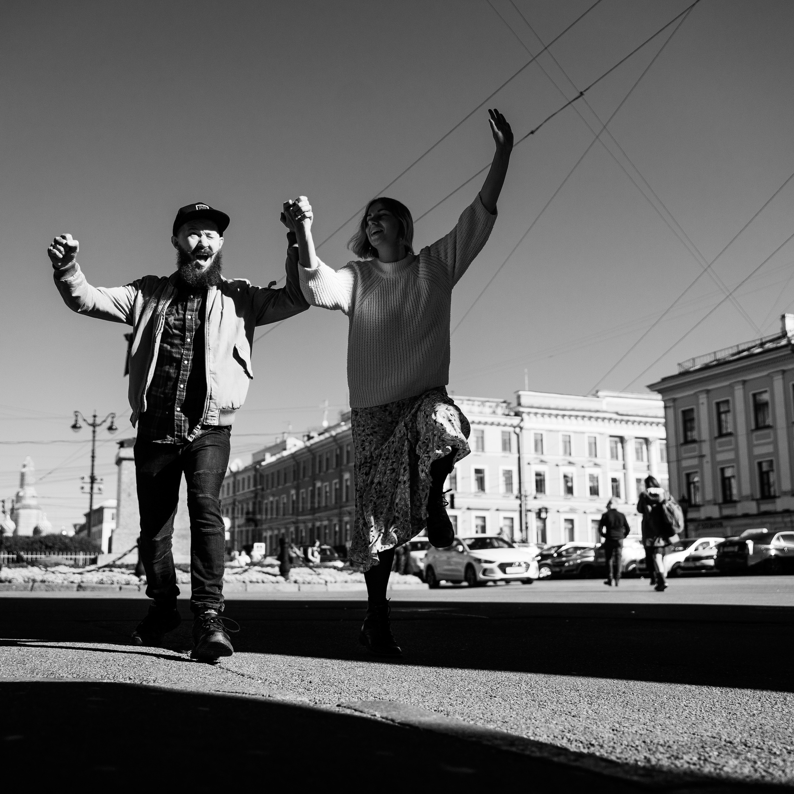 Monochrome image of joyful couple dancing on city streets, high contrast and sharp focus achieved with a fast shutter speed, possibly a 35mm lens to include the urban context