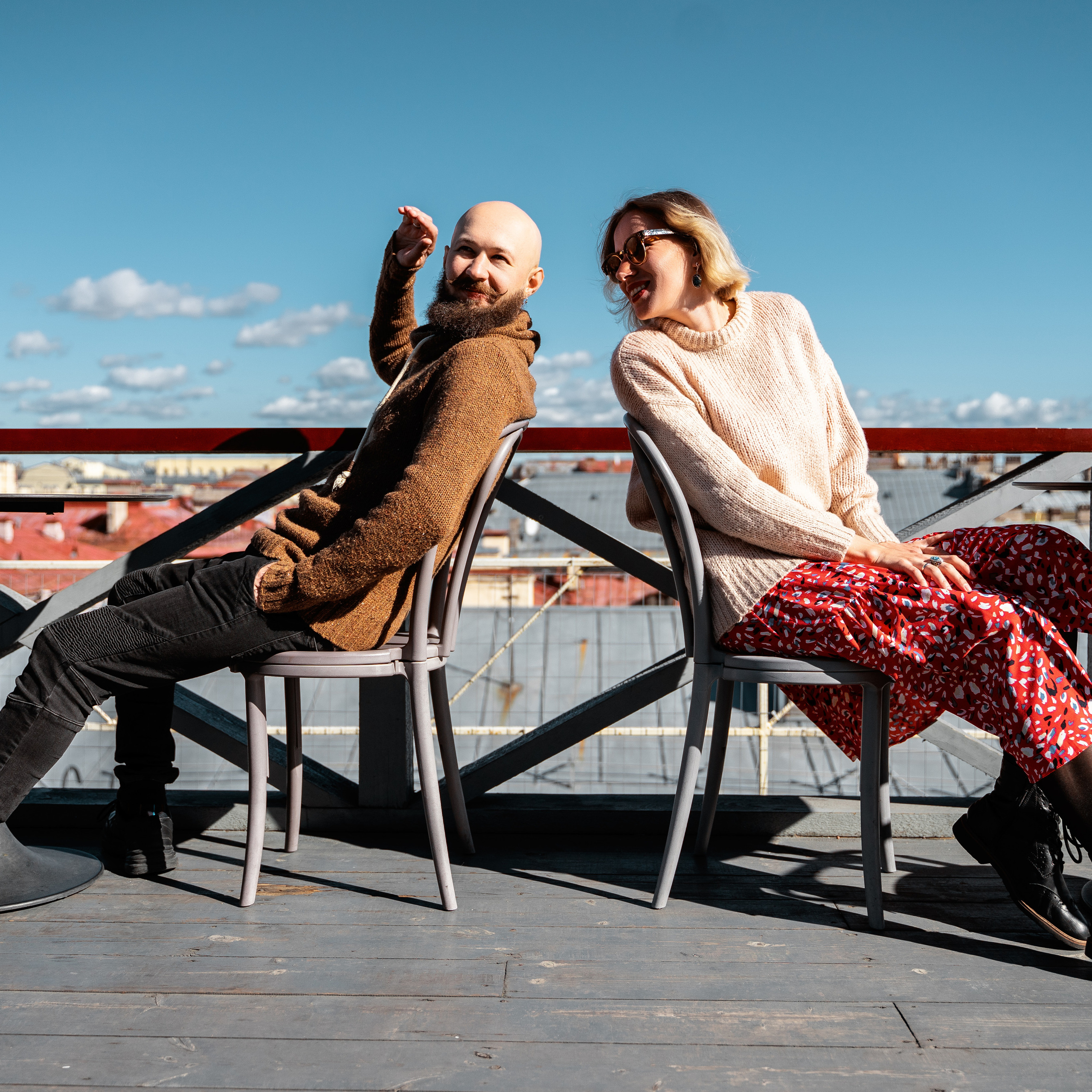 Vibrant couple enjoying sunny rooftop scenery, clear skies in the background, photo likely taken with a wide-angle lens, around 24mm, to capture the expansive cityscape and natural light.
