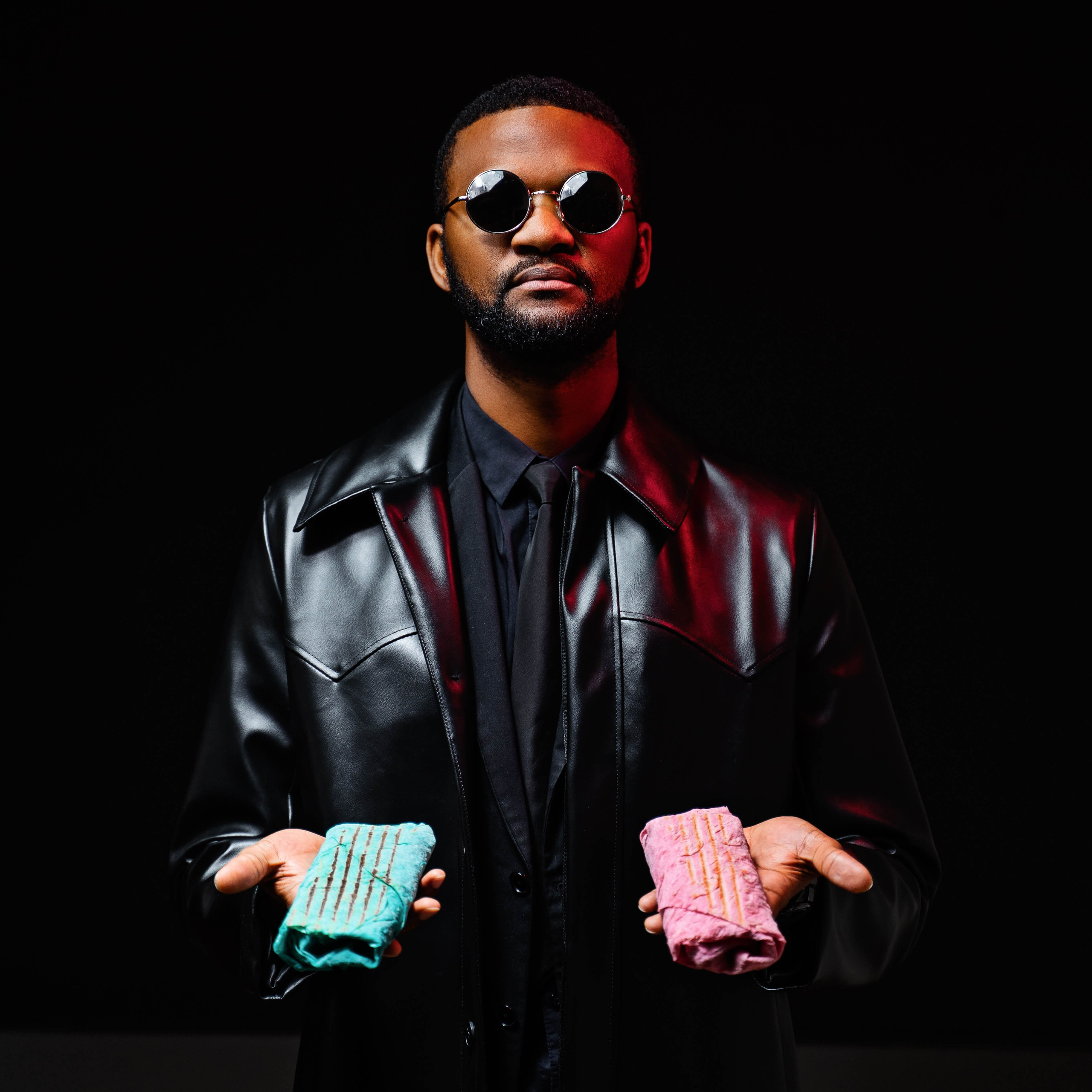A stylish individual in a black leather jacket and round sunglasses, confidently presenting two brightly colored ice cream sandwiches against a stark black background, exuding a cool and enigmatic vibe