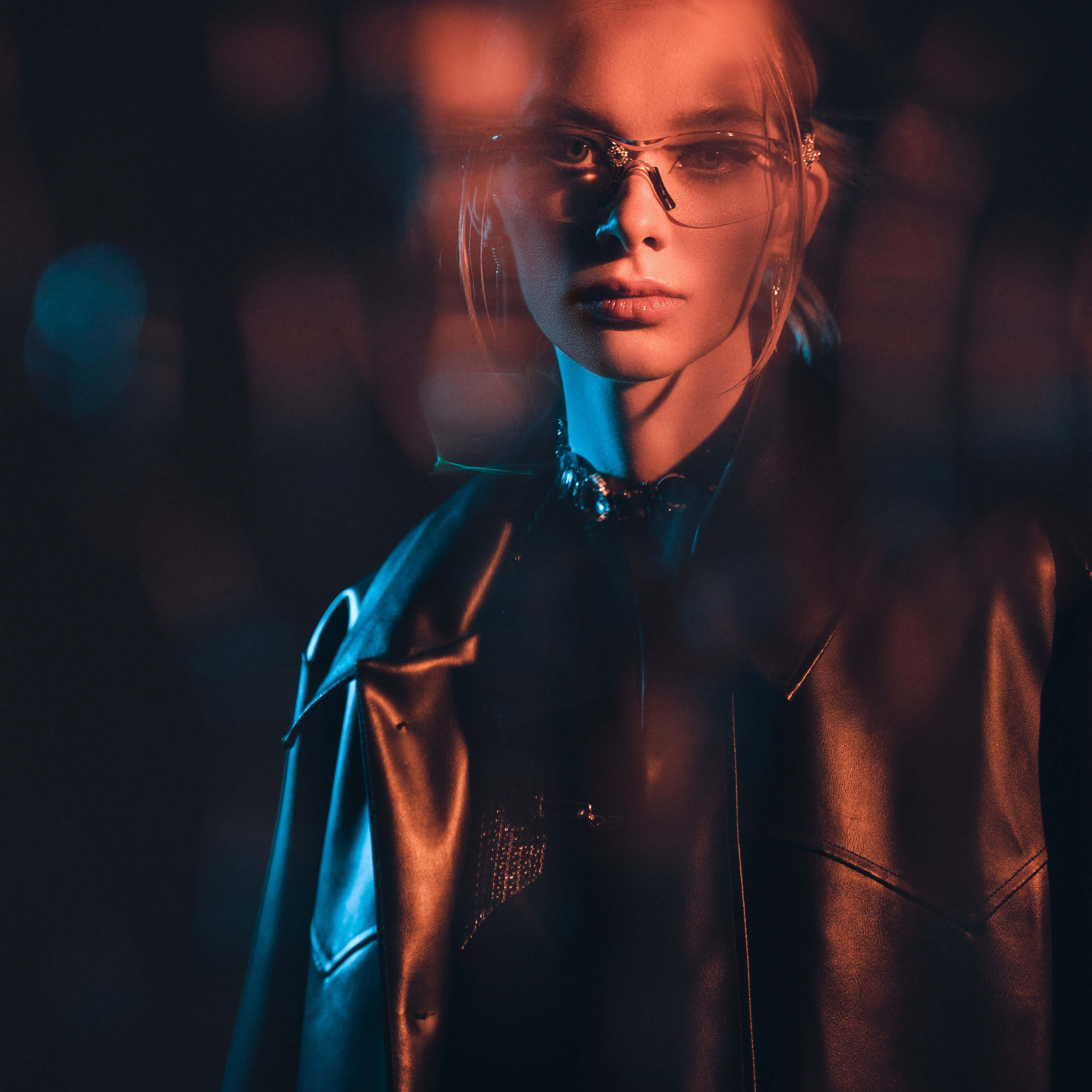A captivating photo capturing a woman's intense look through stylish glasses, highlighted by the interplay of shadow and warm, ambient lighting
