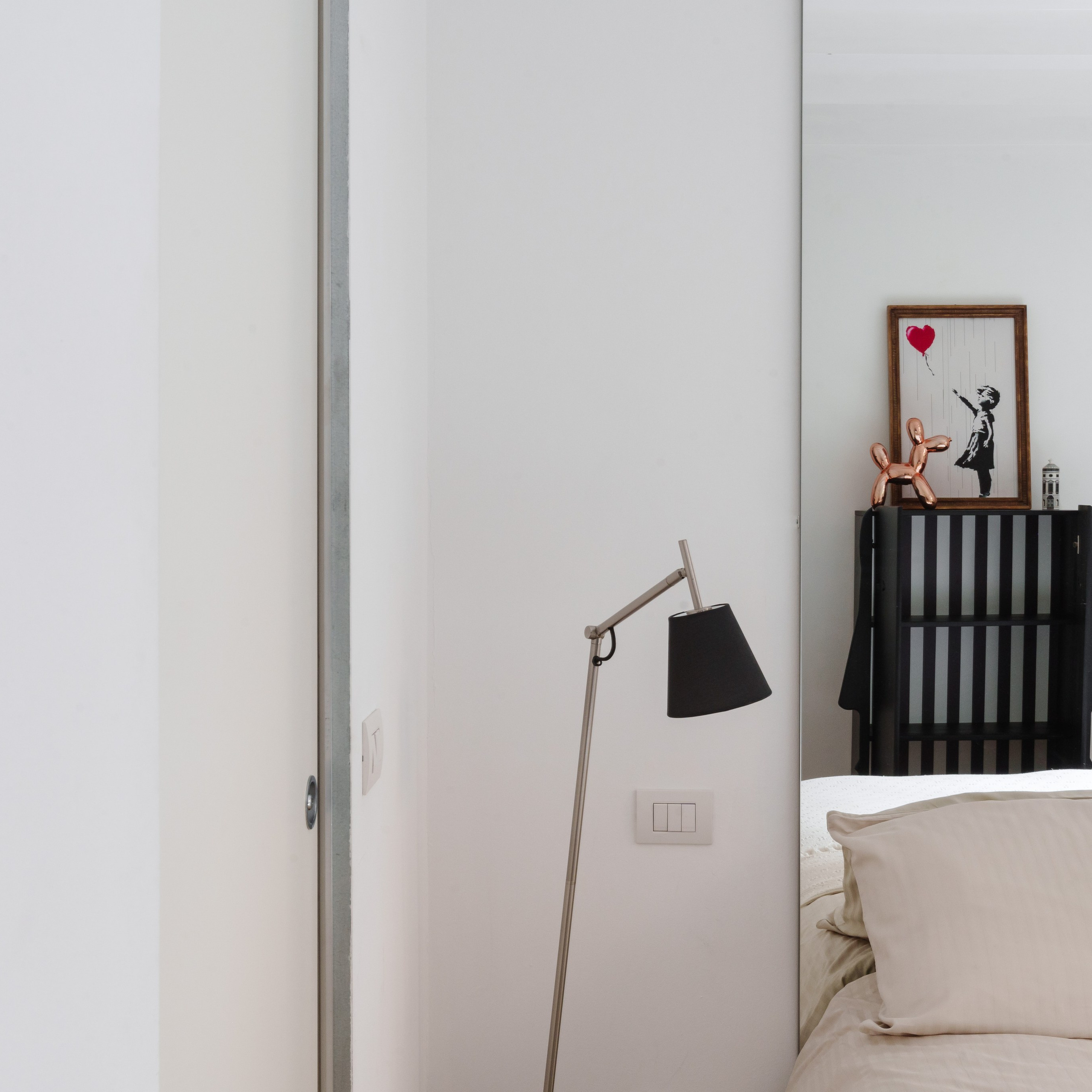 Minimalist bedroom interior with a monochromatic palette, natural light, and a carefully composed art piece and chair in the background, showcasing depth with a narrow aperture lens.