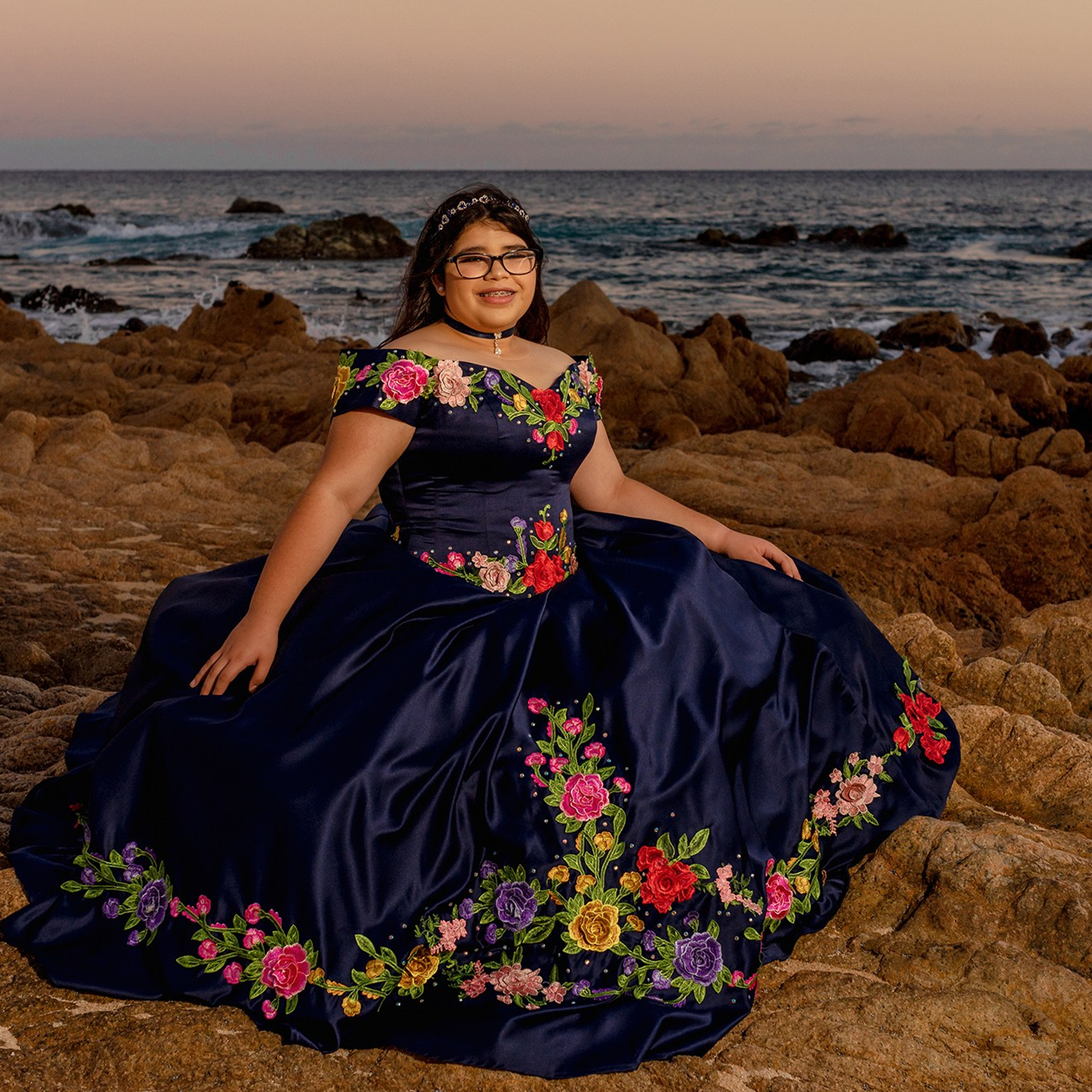 Quinceañera photography in Los Cabos – girl in a traditional Mexican blue dress with floral embroidery, holding a multicolor bouquet during sunset session at Las Viudas beach
