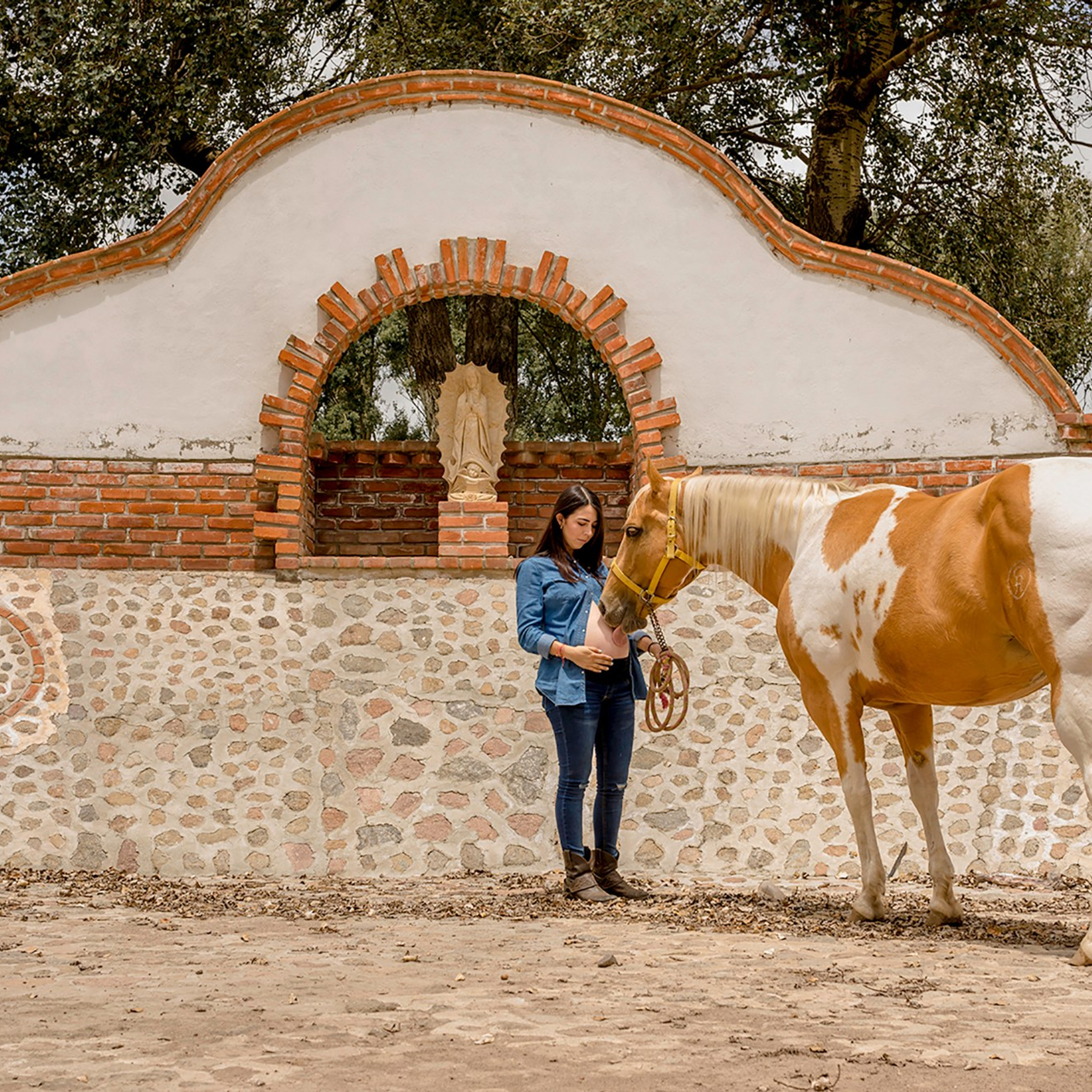 Rustic maternity photography – pregnant woman with her horse in a traditional stone arena, highlighting the beauty of motherhood and anticipation of a new chapter