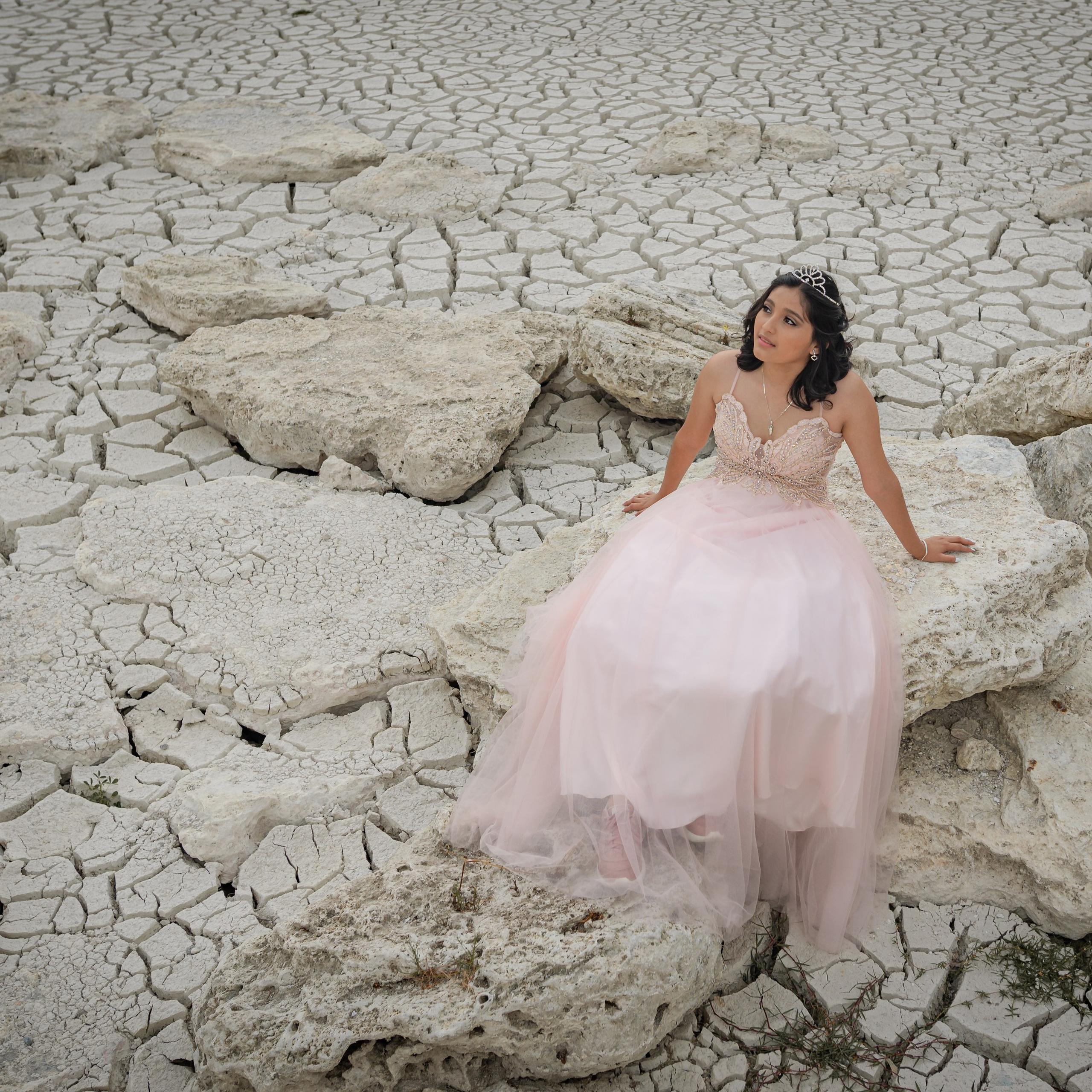 Michelle in a pink dress surrounded by cracked dry land, desert textures, and dramatic arid scenery, captured by destination portrait photographer