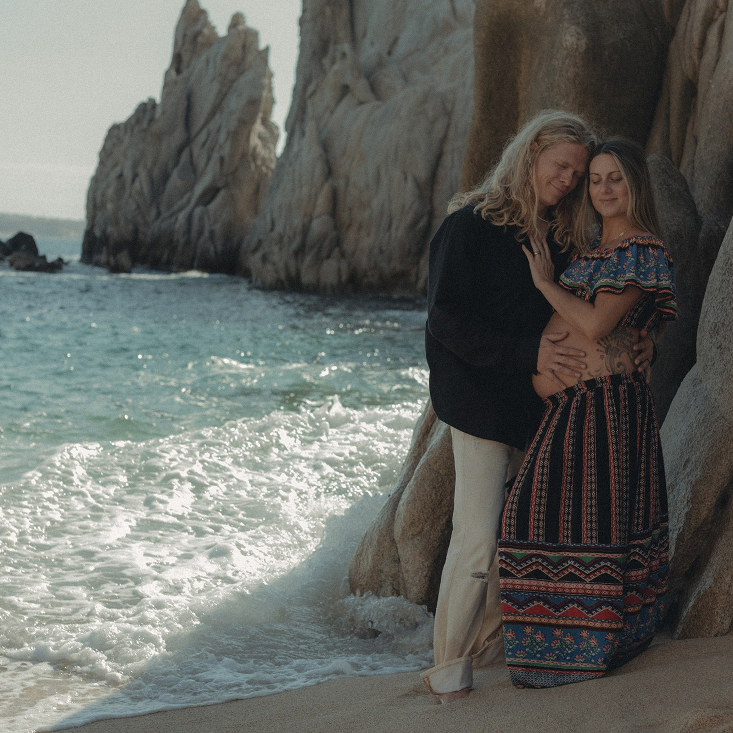 Cinematic maternity portraits in Cabo San Lucas – mother-to-be at Playa del Amor with dramatic rocks and beach scenery, edited with cinematic tones, professional maternity and family photographer