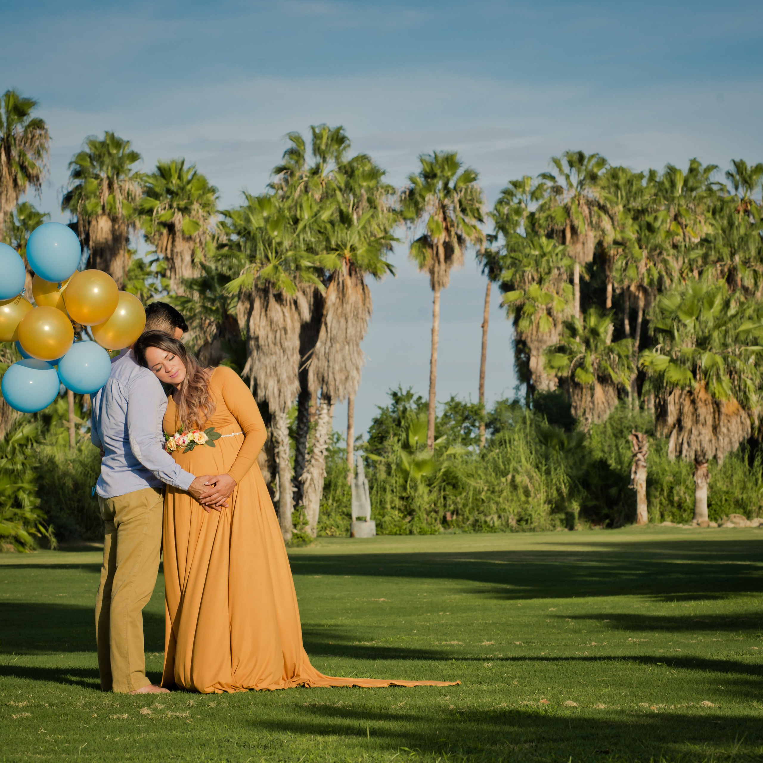 Maternity couple photoshoot in Los Cabos – expecting parents embracing by the ocean, hands on baby bump, with palm trees and beach backdrop, captured by Baja California Sur photographer