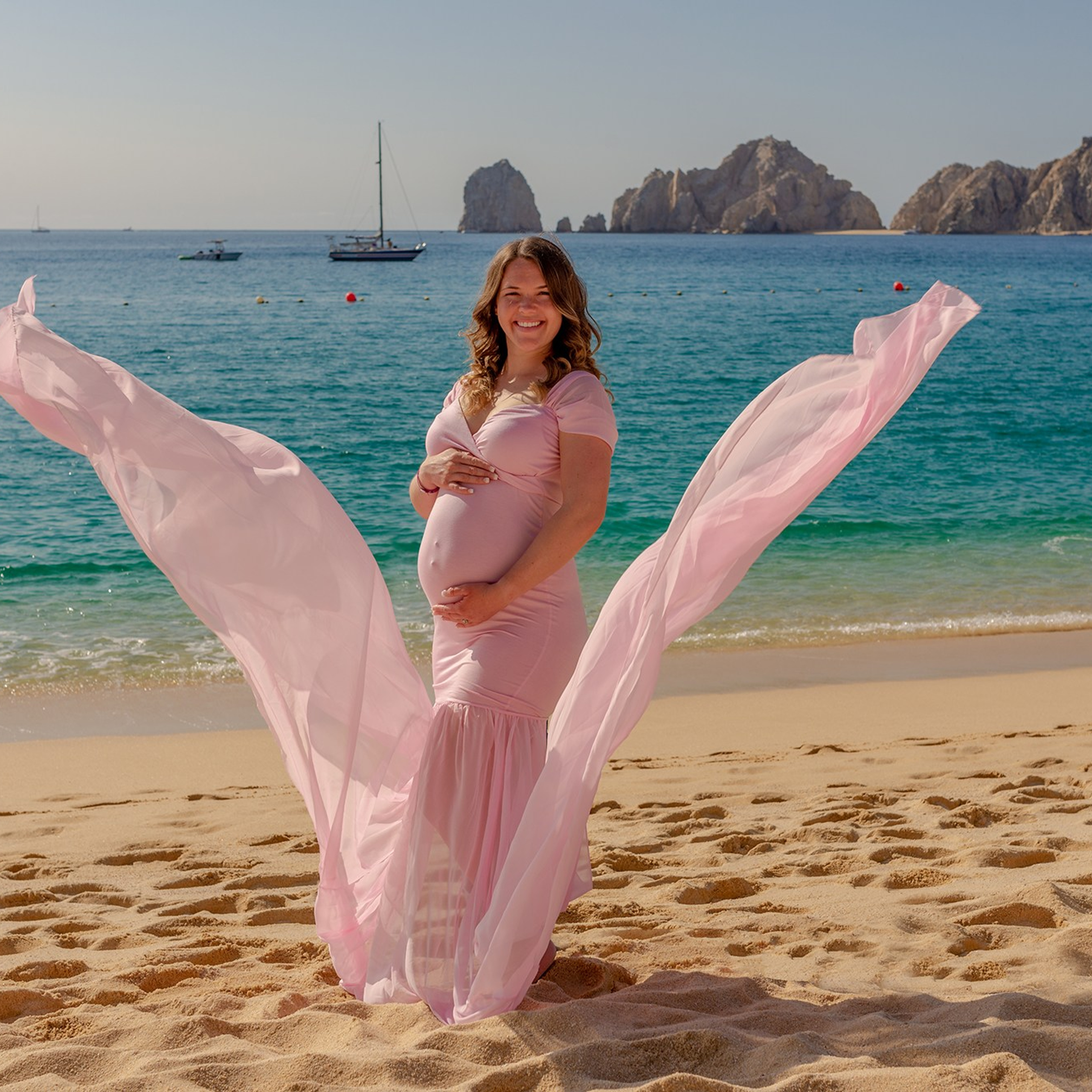 Los Cabos maternity photographer – elegant portrait of expecting mother in a dress flowing in the wind, highlighting the love, strength, and beauty of pregnancy by the sea