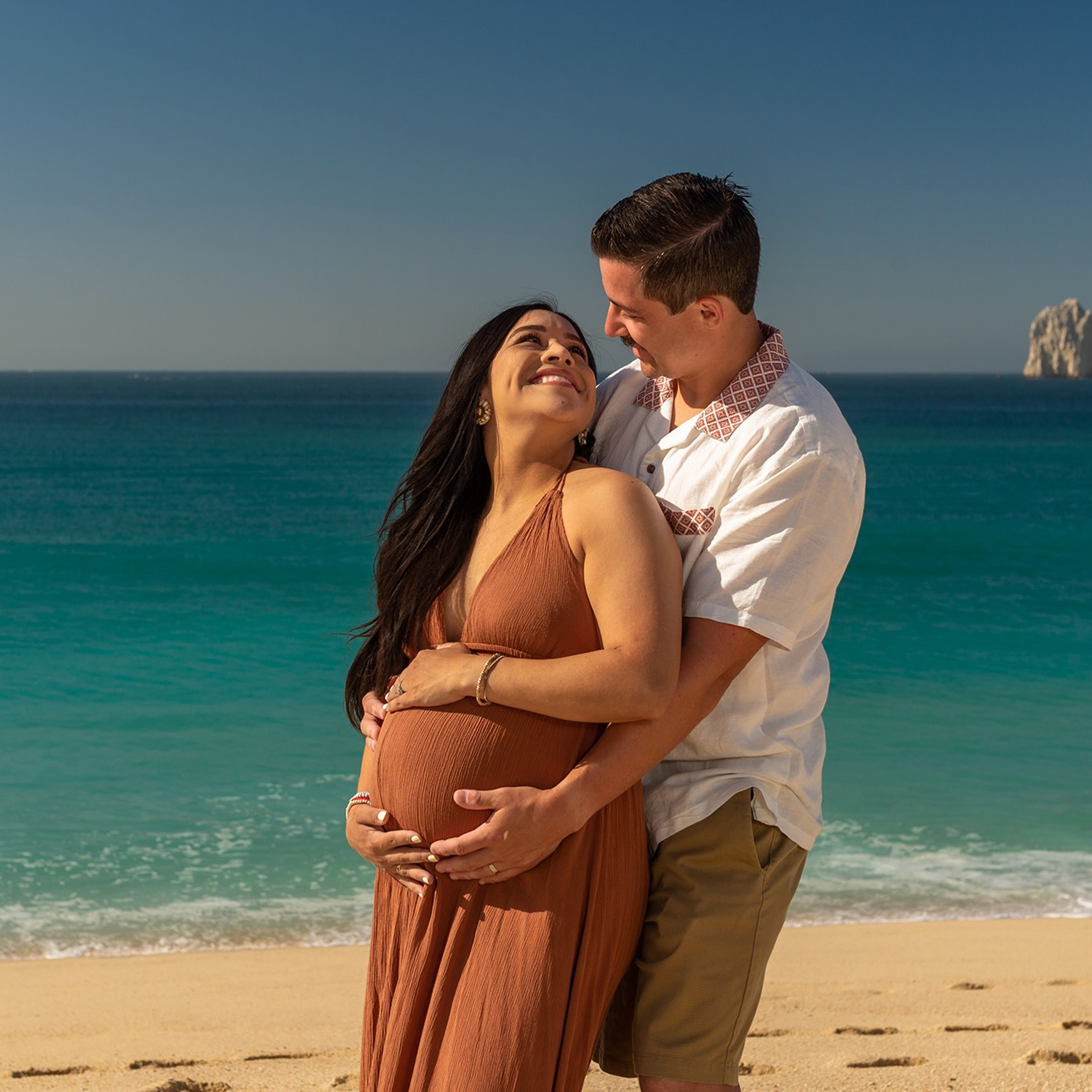 Maternity photography in Baja California Sur – intimate portrait of expecting mother by the sea, hands on her belly, representing love and the miracle of life