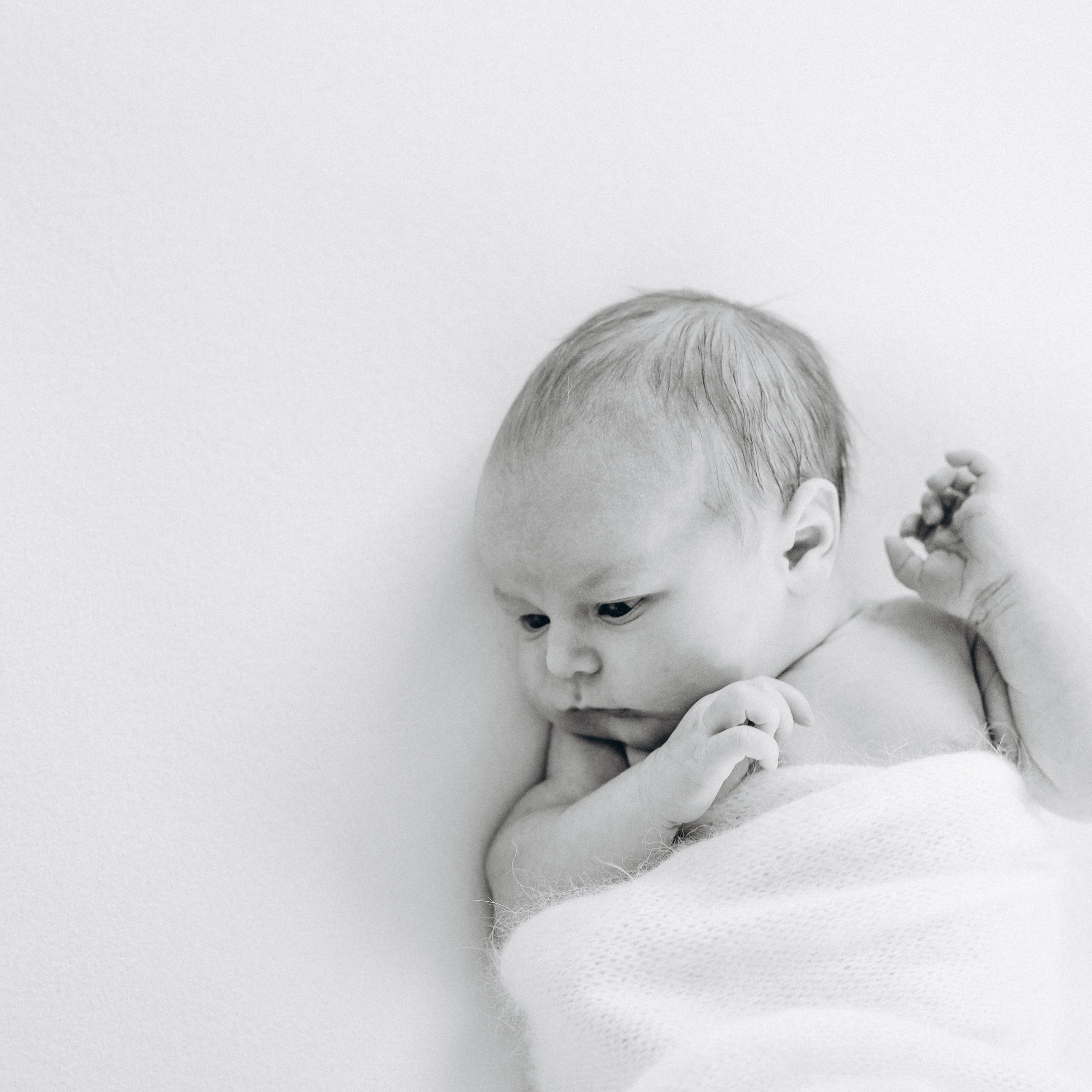 Ein neugeborenes Mädchen gewickelt in einen flauschigen Wrap aus Strick schaut zur Seite.