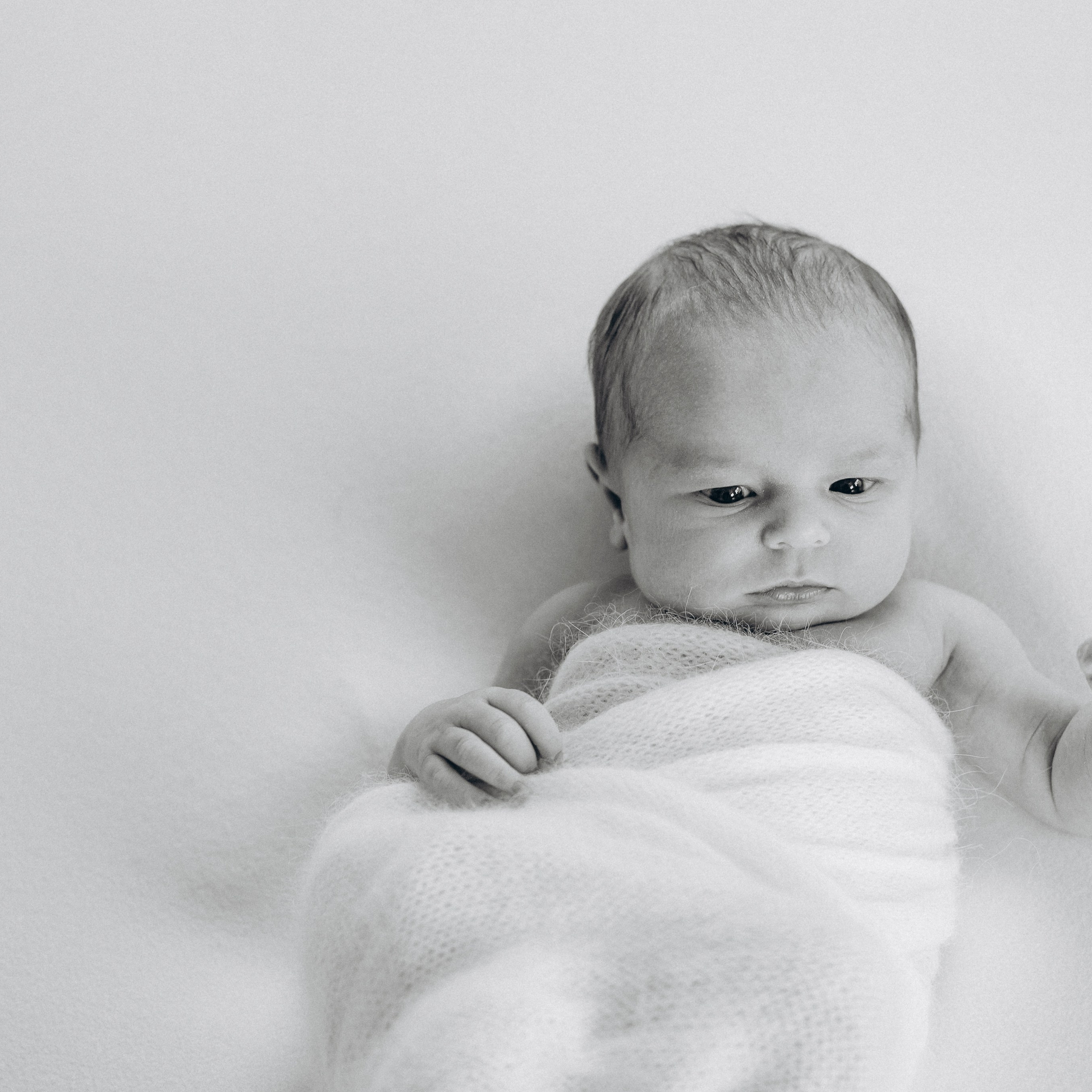 Ein niedliches neugeborenes Mädchen in einen Wrap gewickelt schaut in die Kamera. Newborn, Lifestyle, Osnabrück, Newbornshooting, Homestory.