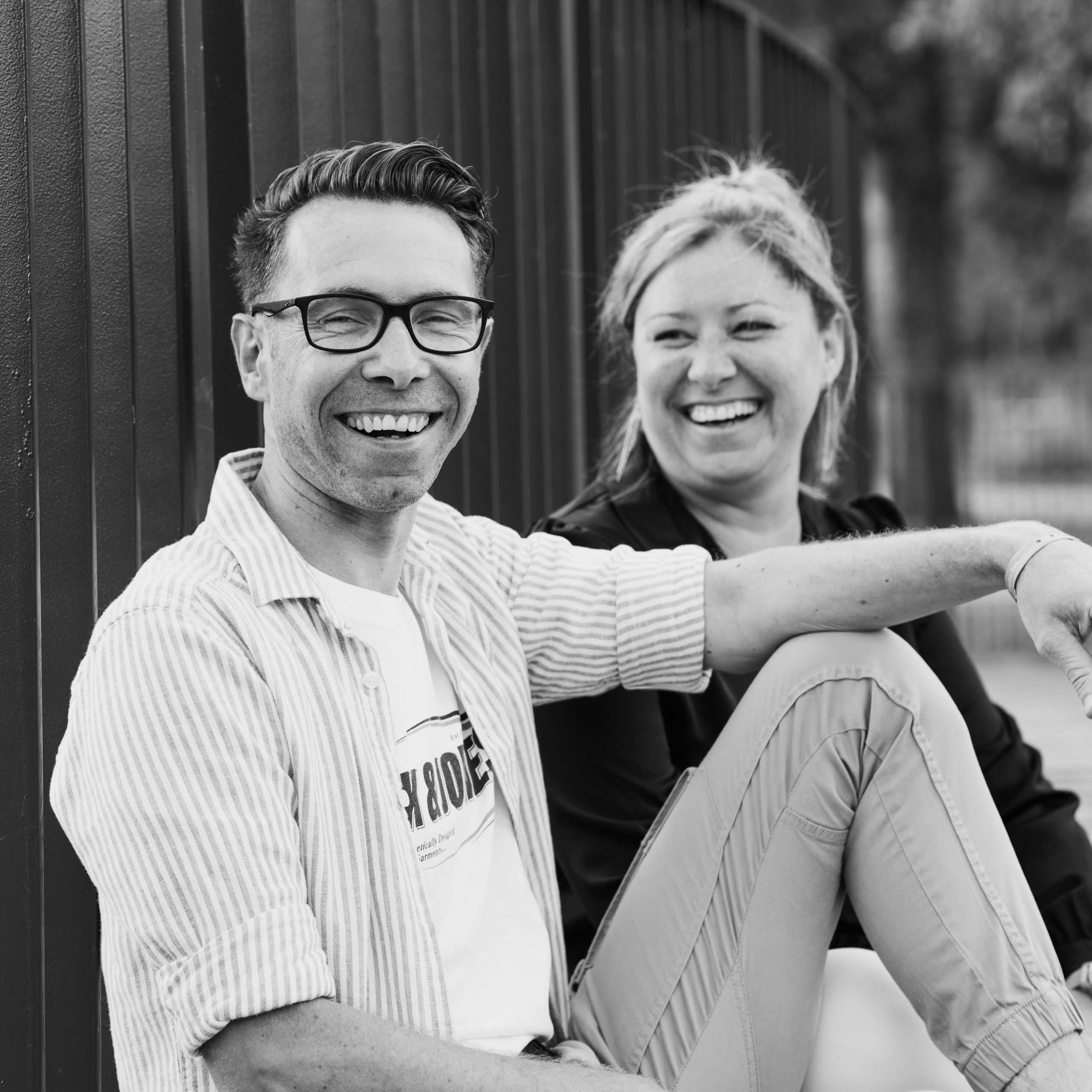 Zwart-wit foto van broer en zus zittend naast elkaar en lachend tijdens spontane familieshoot door Kapture Fotografie