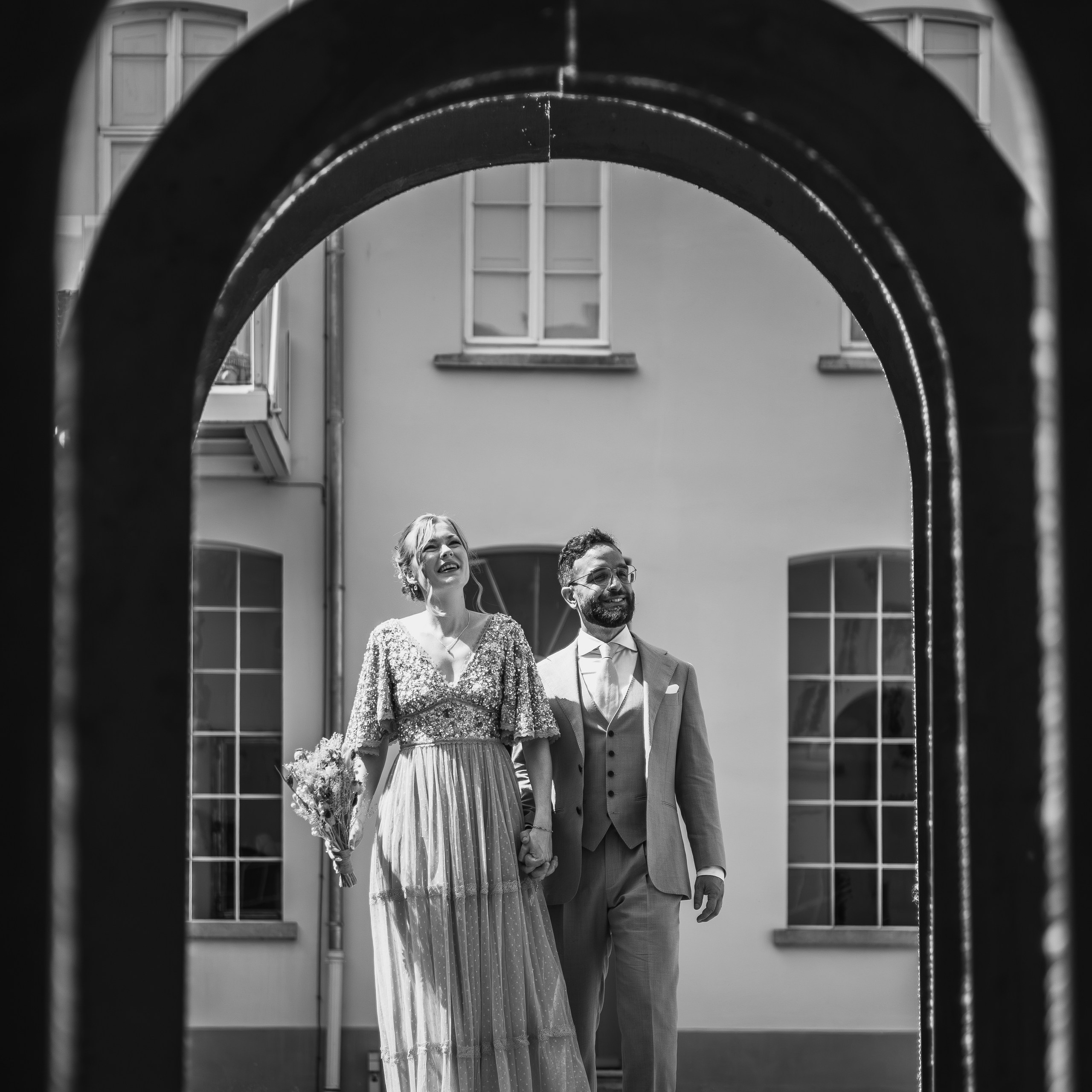 Zwart-wit foto van bruid en bruidegom lopend door een boog tijdens romantische trouwshoot vastgelegd door Kapture Fotografie