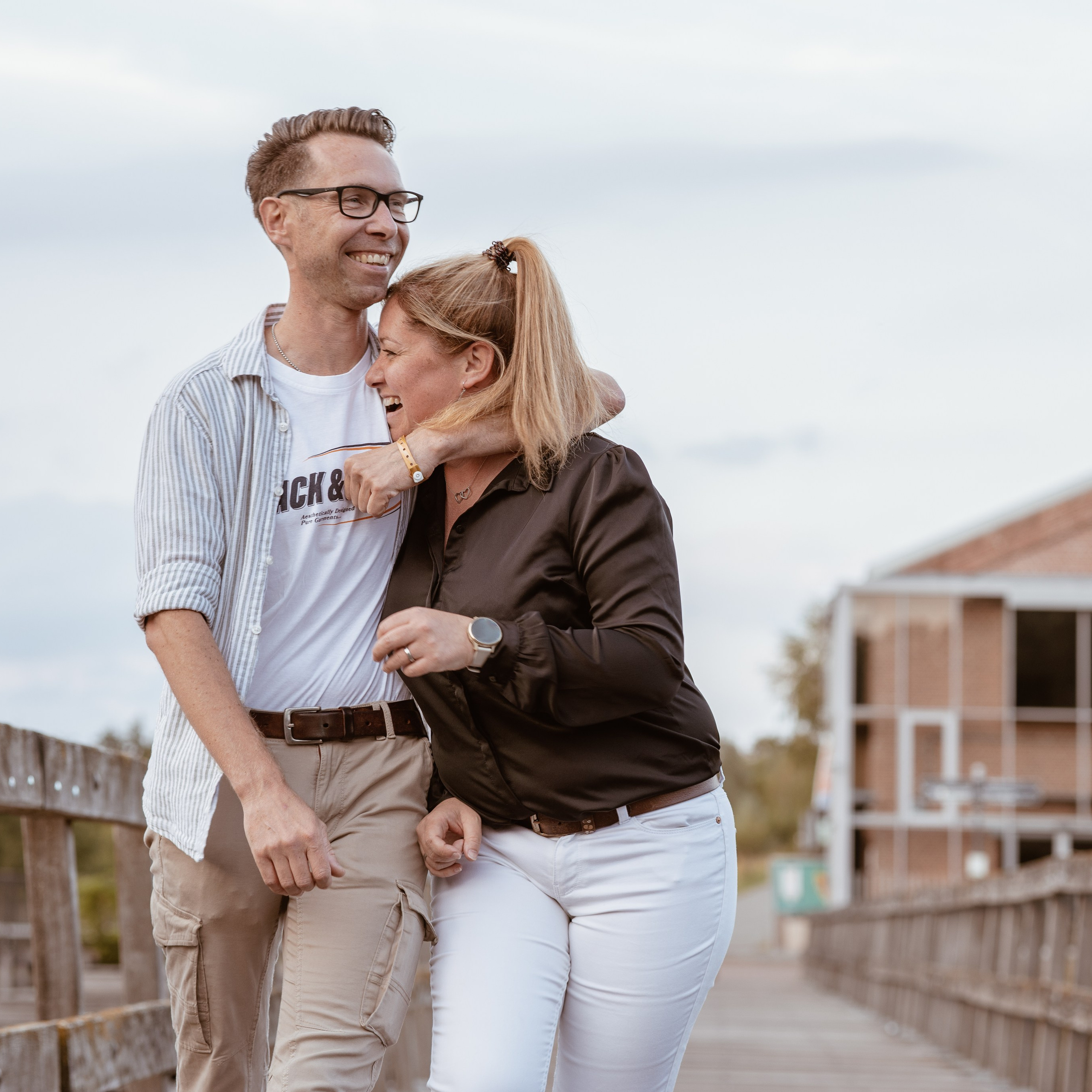 Broer en zus wandelen lachend over een brug tijdens spontane buitenfotoshoot door Kapture Fotografie