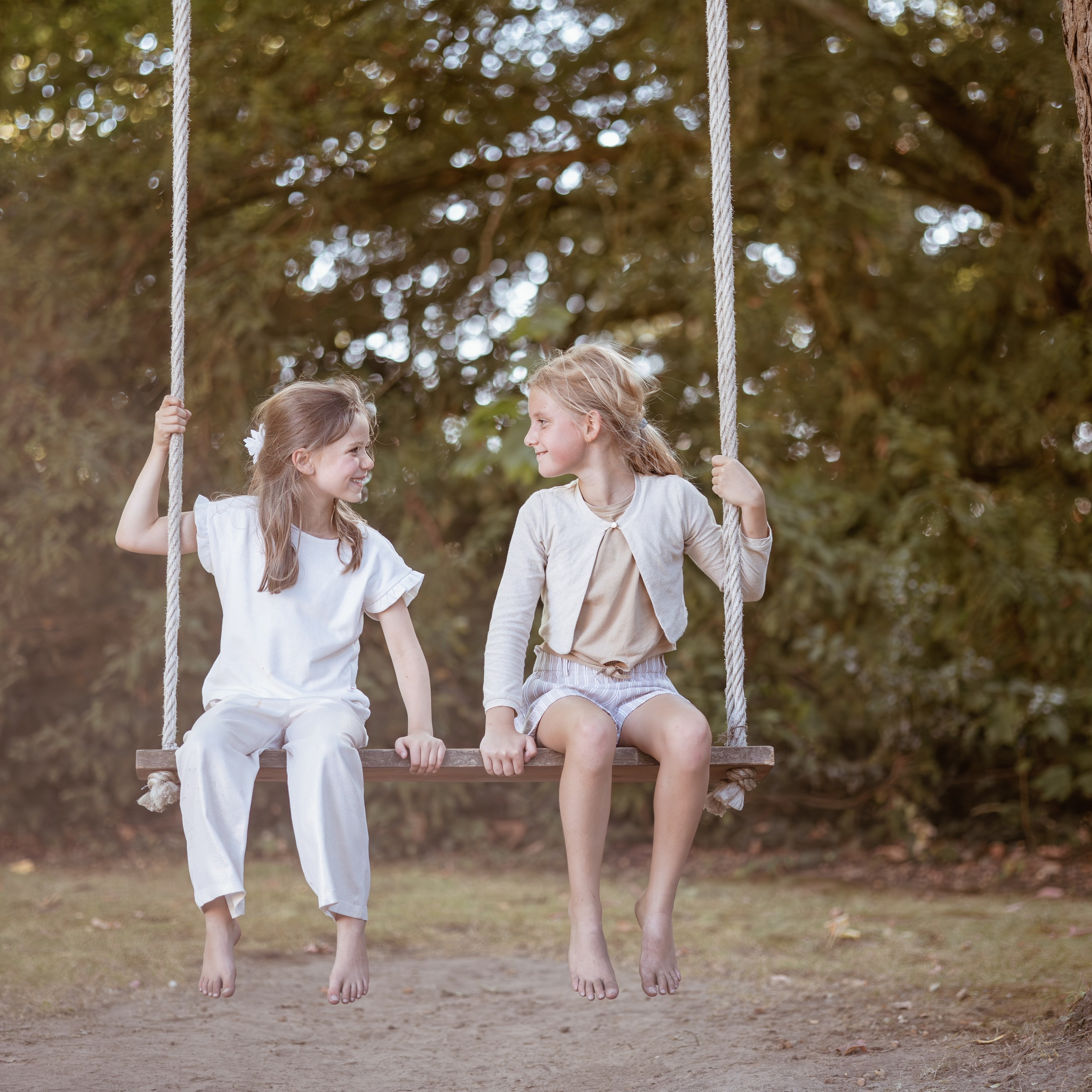 Twee meisjes op een schommel tijdens zonsondergang vastgelegd in warm natuurlijk licht door Kapture Fotografie