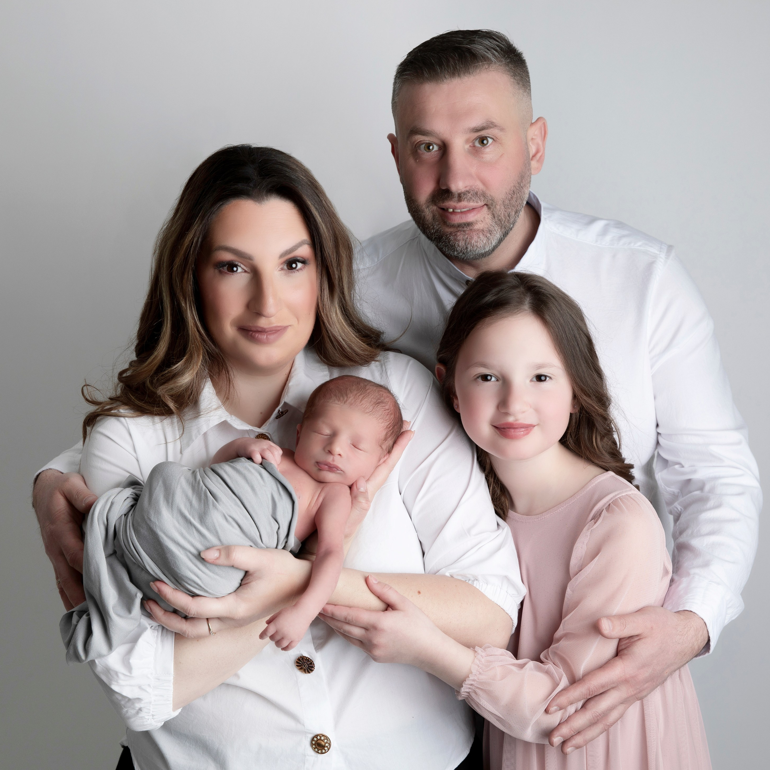 "Familjefotografi som visar föräldrar med deras nyfödda baby och äldre syskon. Bilden fångar den kärleksfulla och glada familjebanden samt den speciella stunden av att välkomna ett nytt familjemedlem."